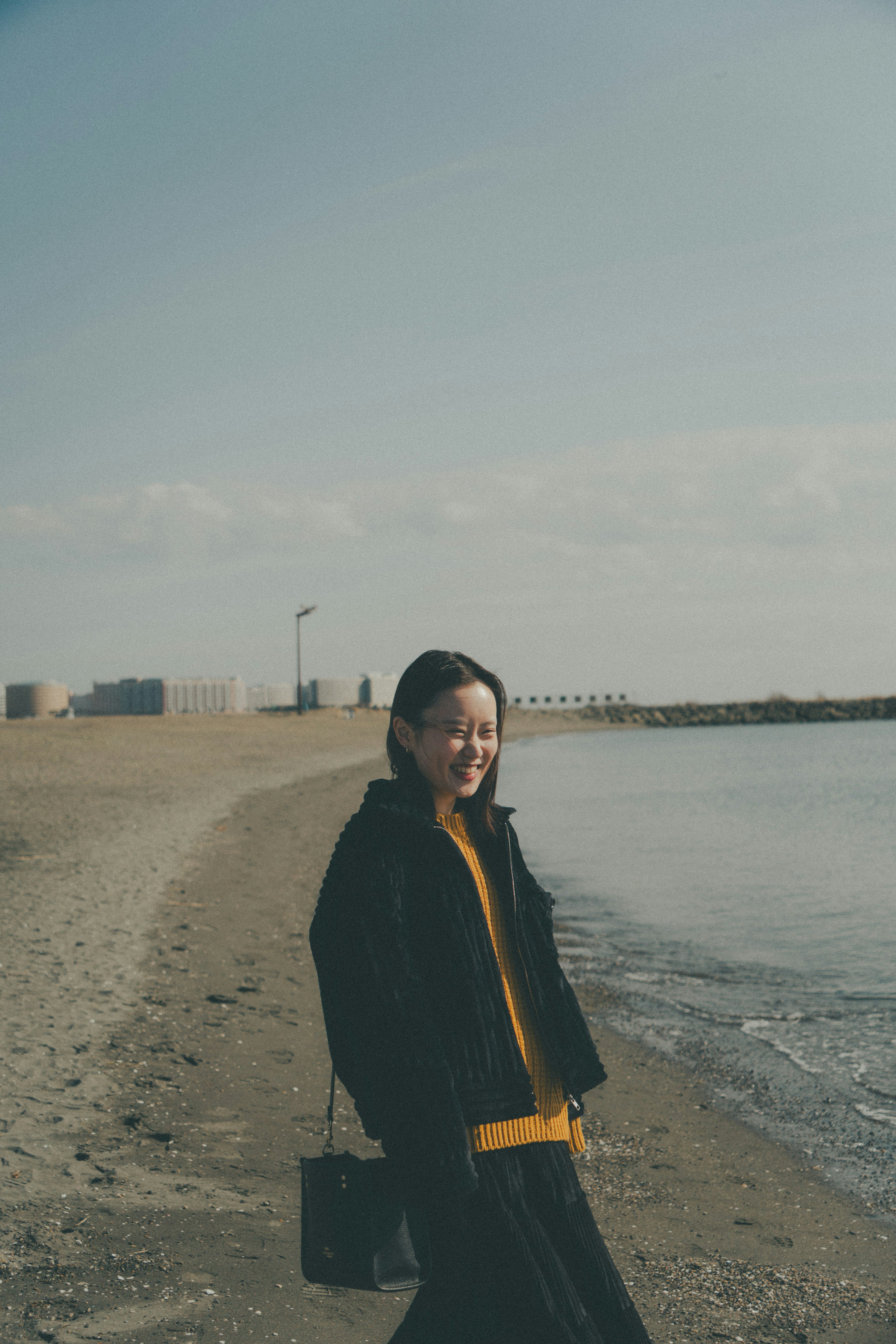 Eine lächelnde Frau am Strand in schwarzer Jacke und gelbem Pullover