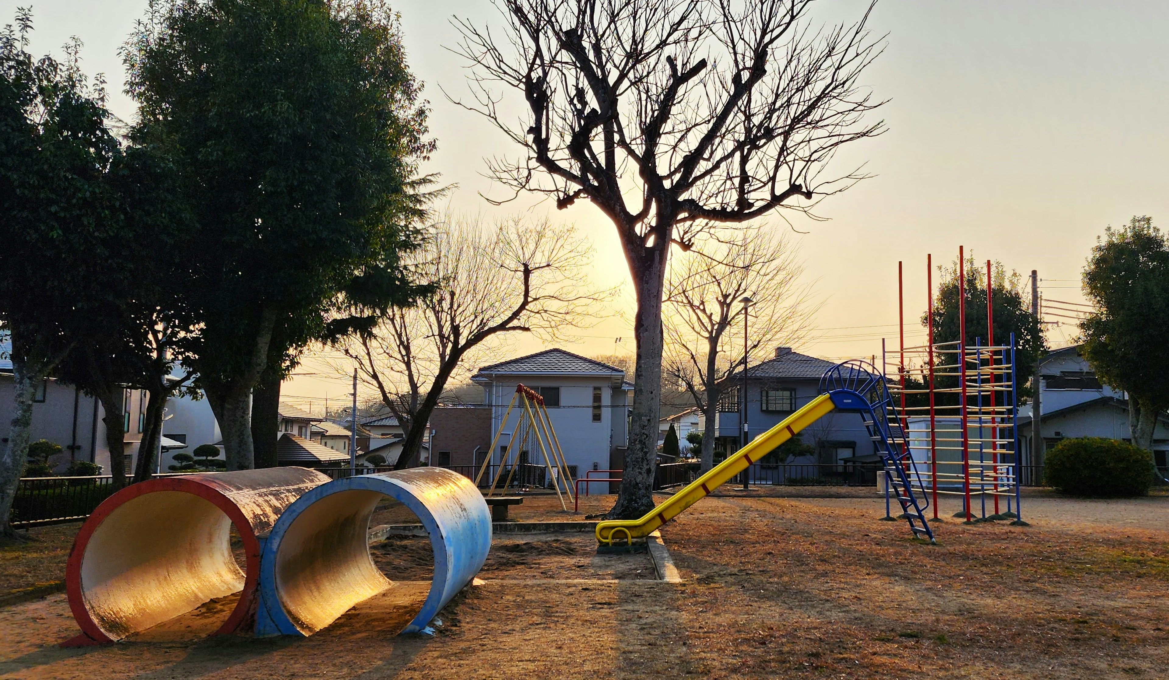 Scena di parco giochi con tunnel rossi e blu scivolo giallo albero spoglio cielo al tramonto