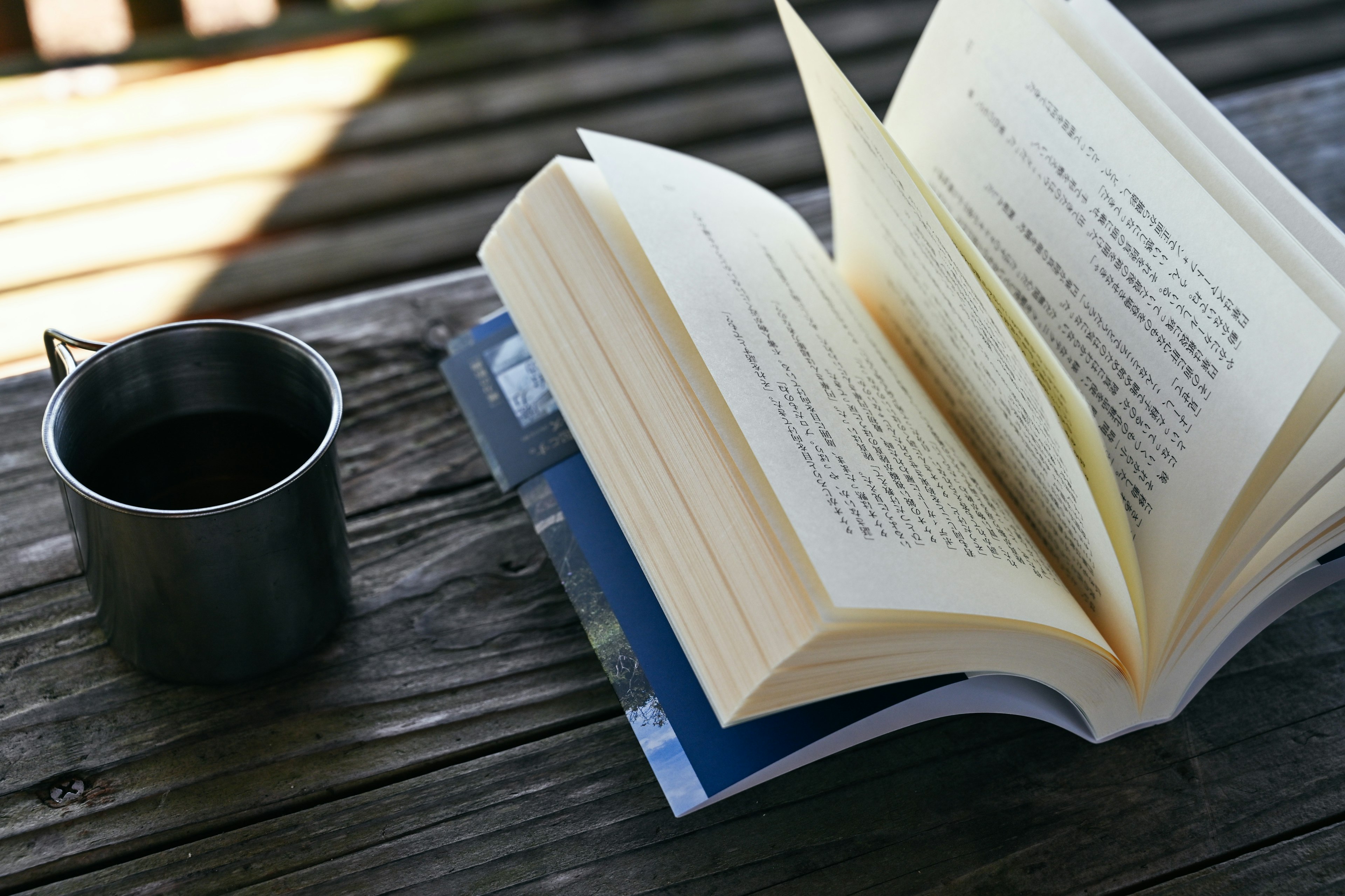 Ein offenes Buch und eine Metalltasse auf einem Holztisch