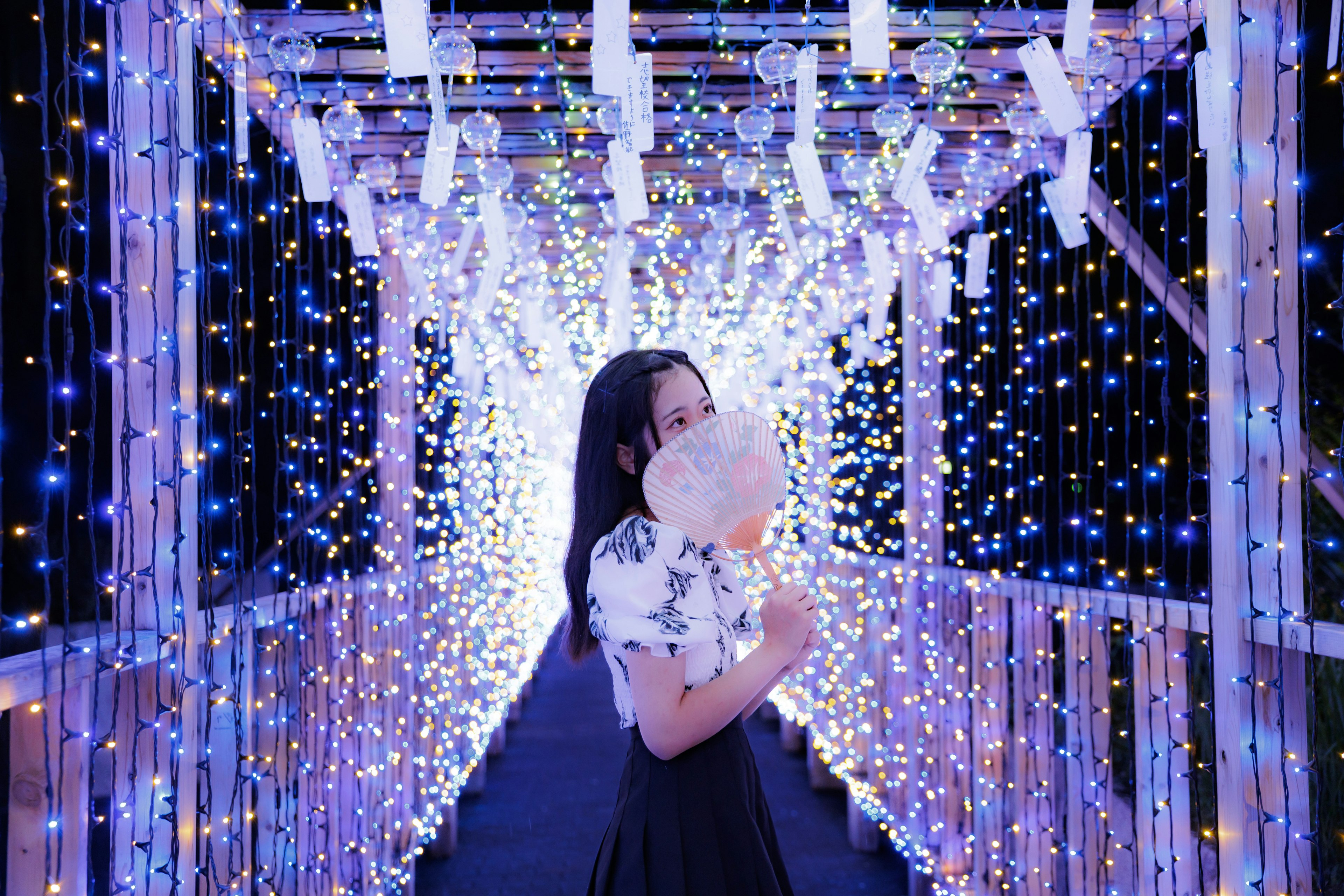 Una donna in piedi su un ponte splendidamente illuminato che tiene un ventaglio indossando un vestito bianco