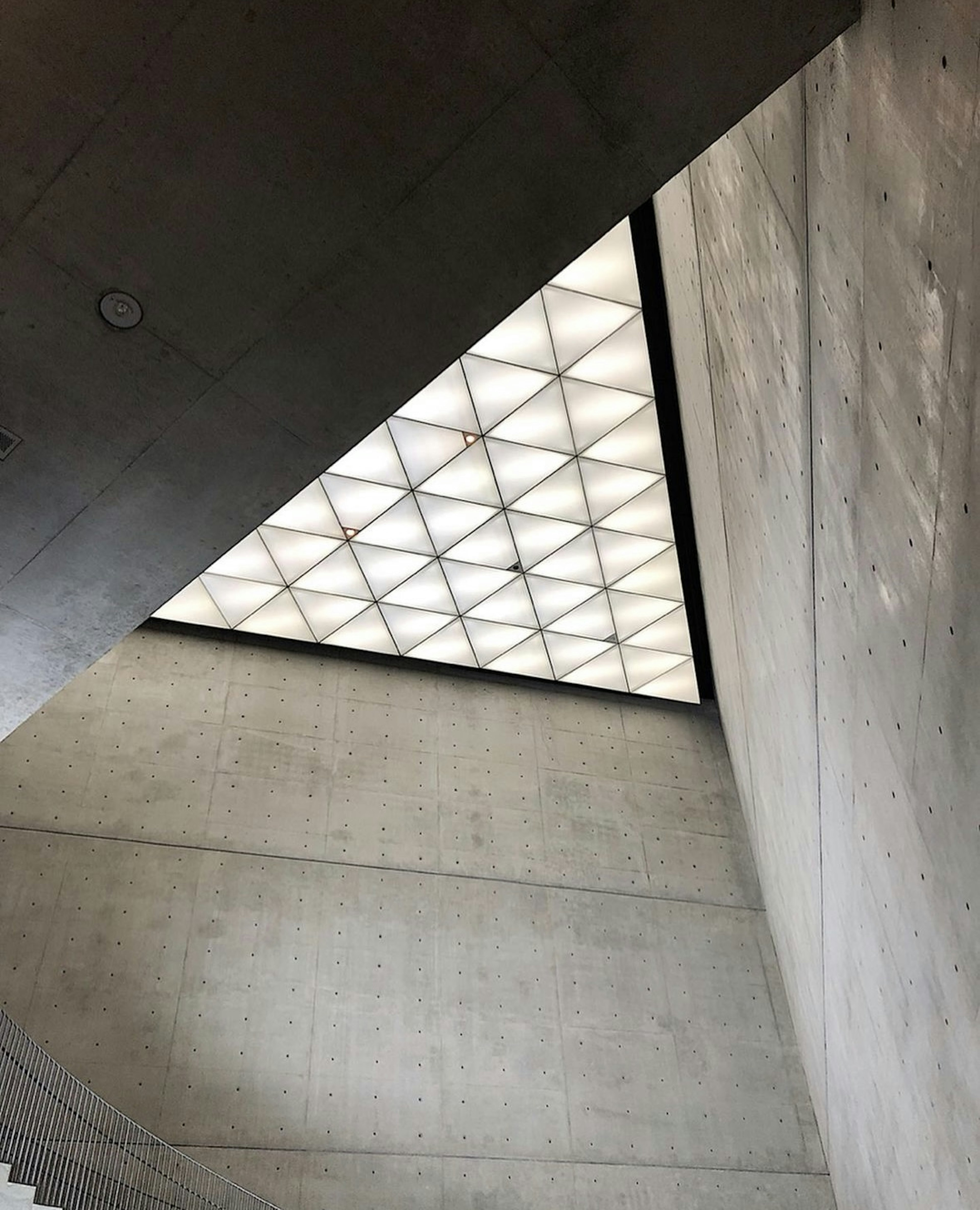 View from a staircase looking up at a triangular ceiling design and concrete walls