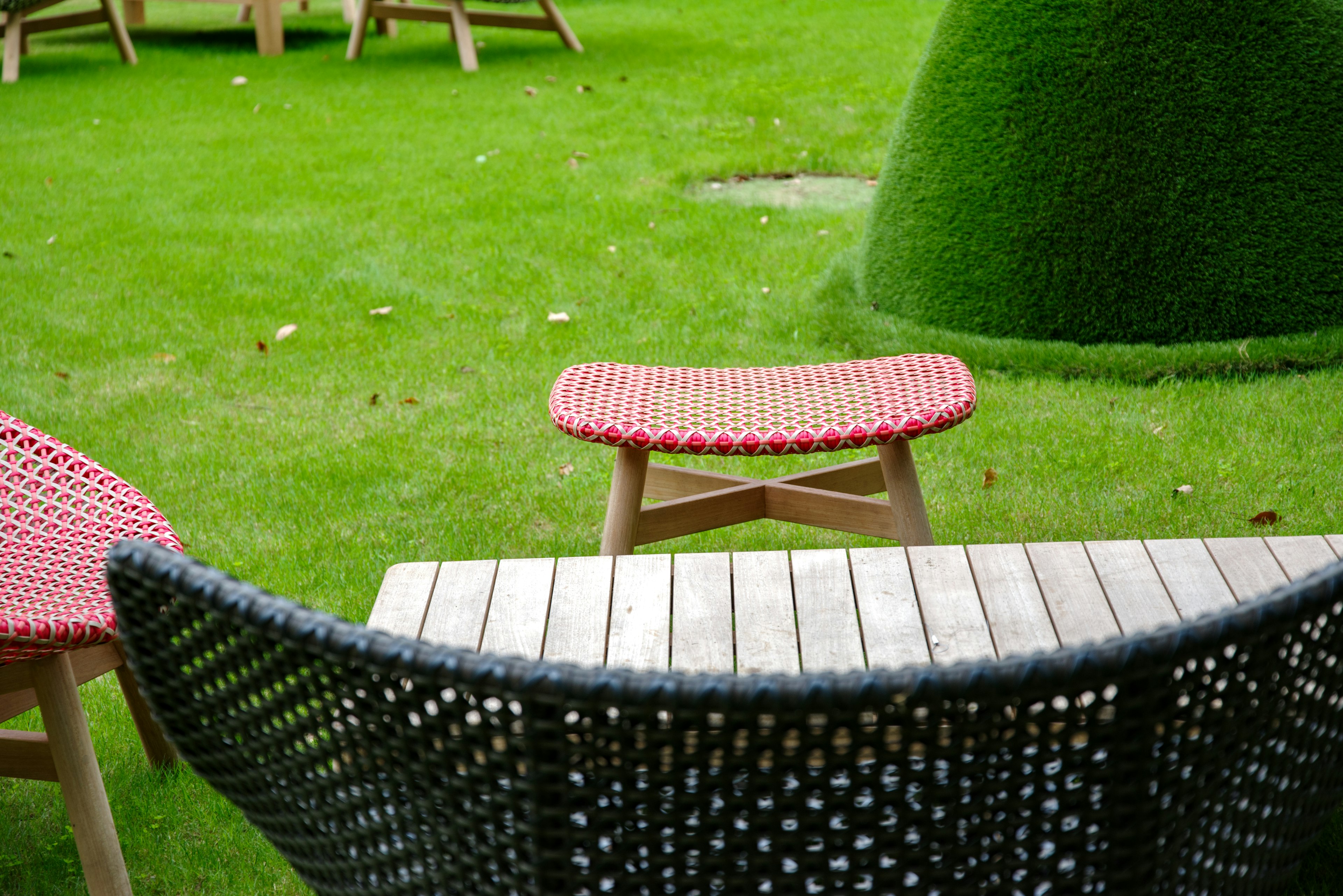 Black woven chair and table with red cushion on green grass