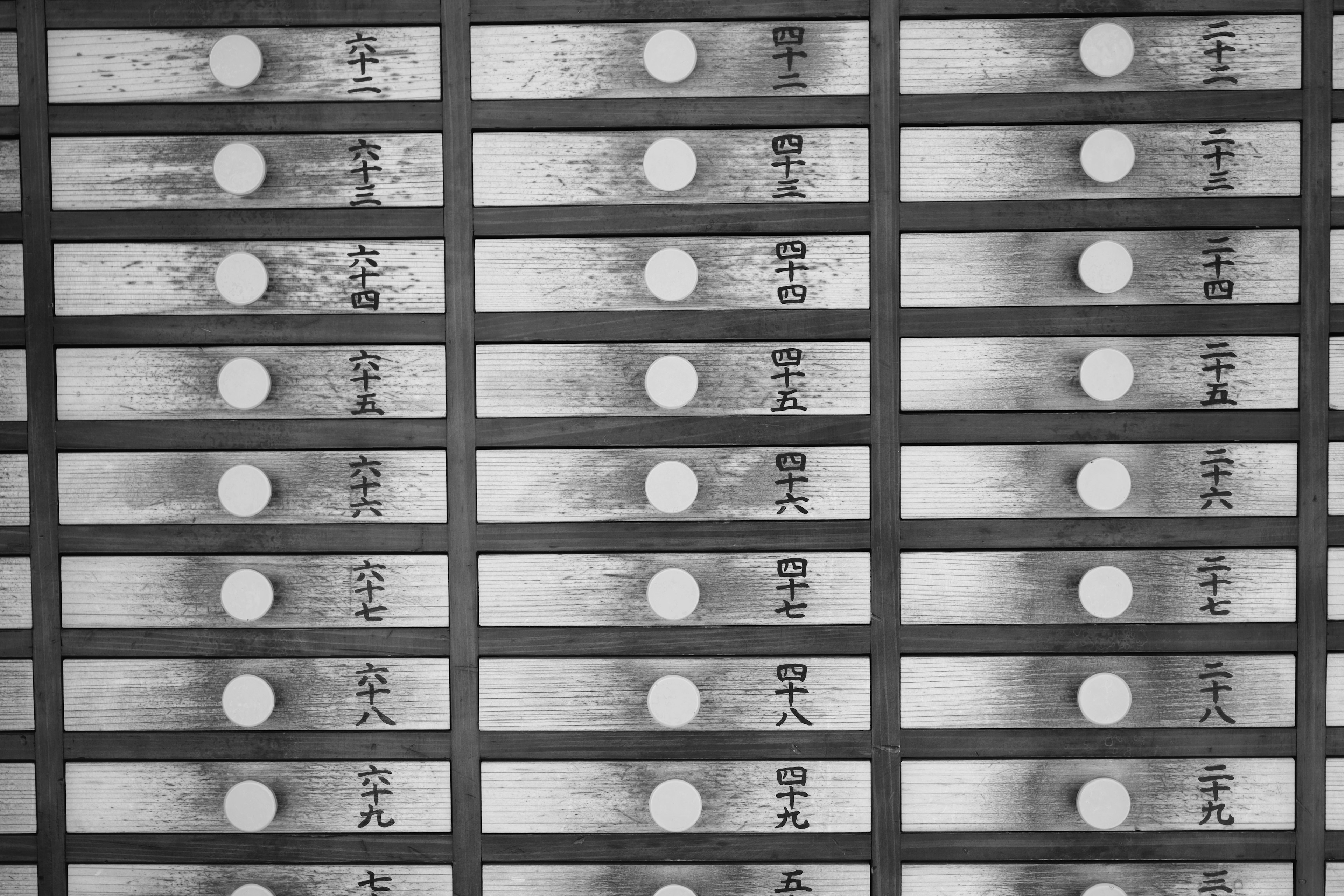 Black and white image of wooden drawers arranged in rows Each drawer features a round handle with Japanese characters inscribed