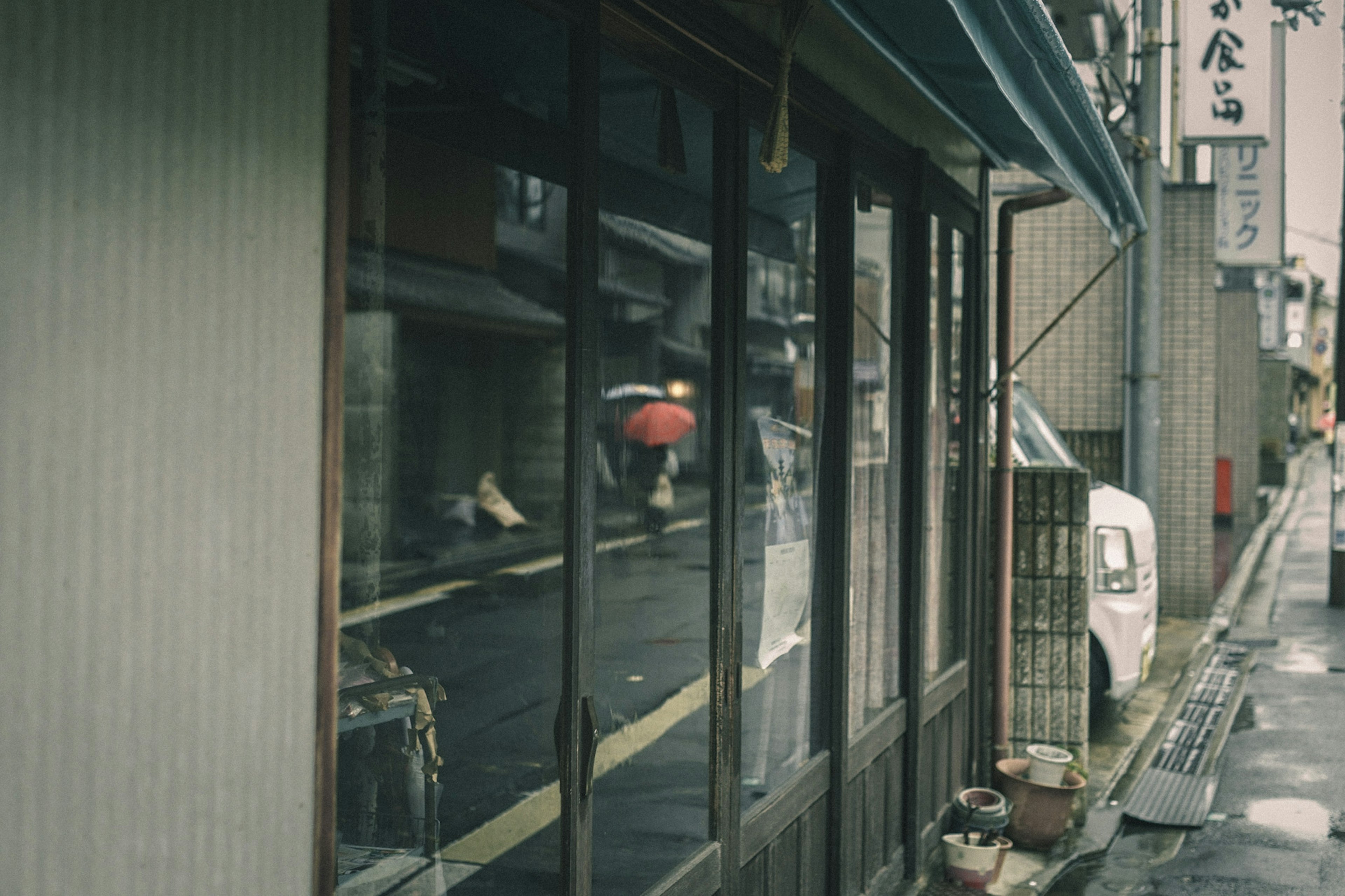 A corner of an old Japanese street with a person holding an umbrella in front of a shop window