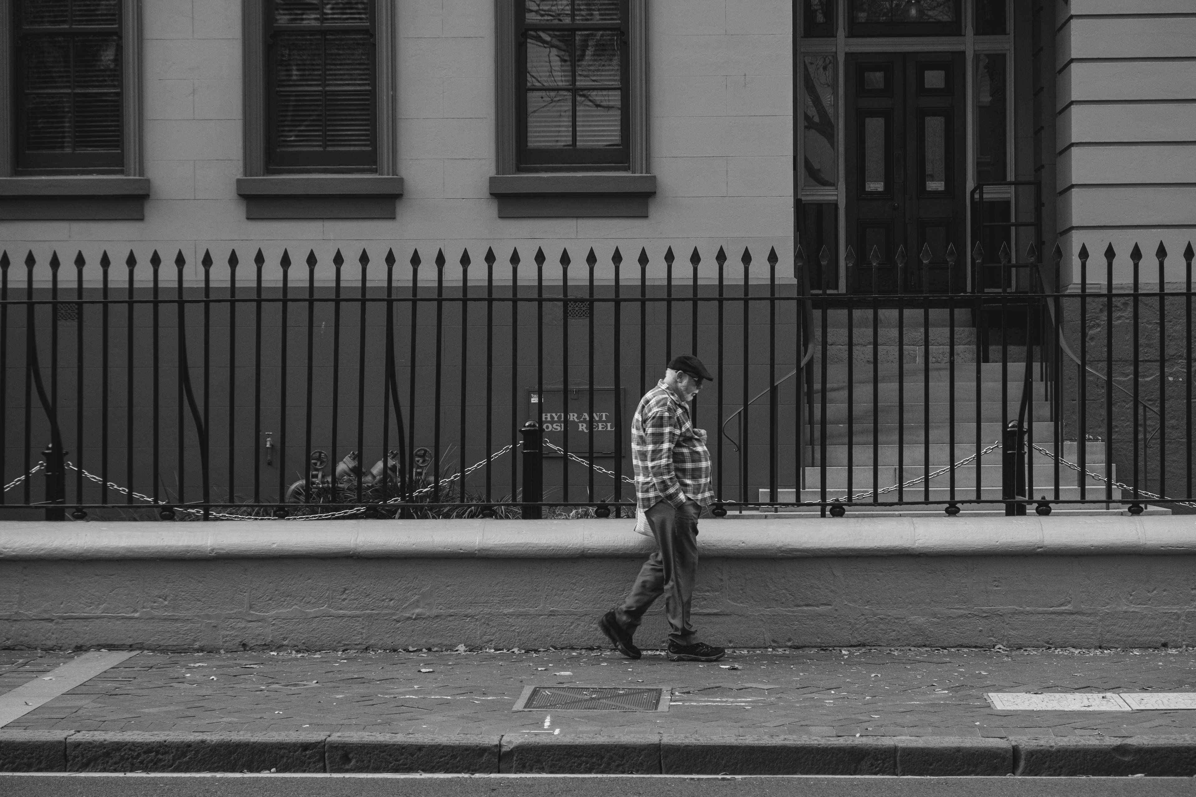 Hombre caminando en una calle en blanco y negro junto a la cerca de un edificio histórico