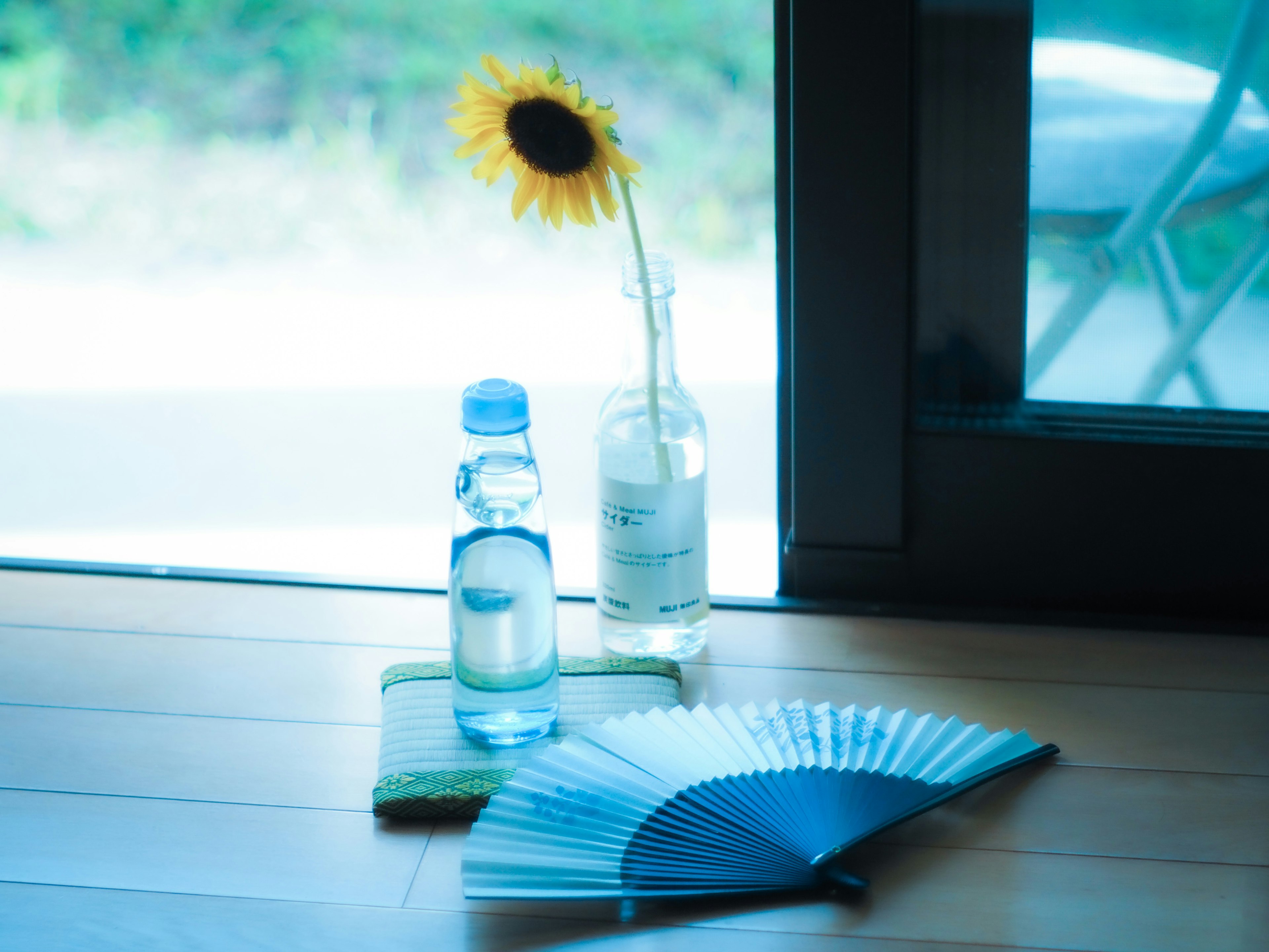 花瓶に入ったひまわりと水のボトルが置かれた窓辺の静かなシーン