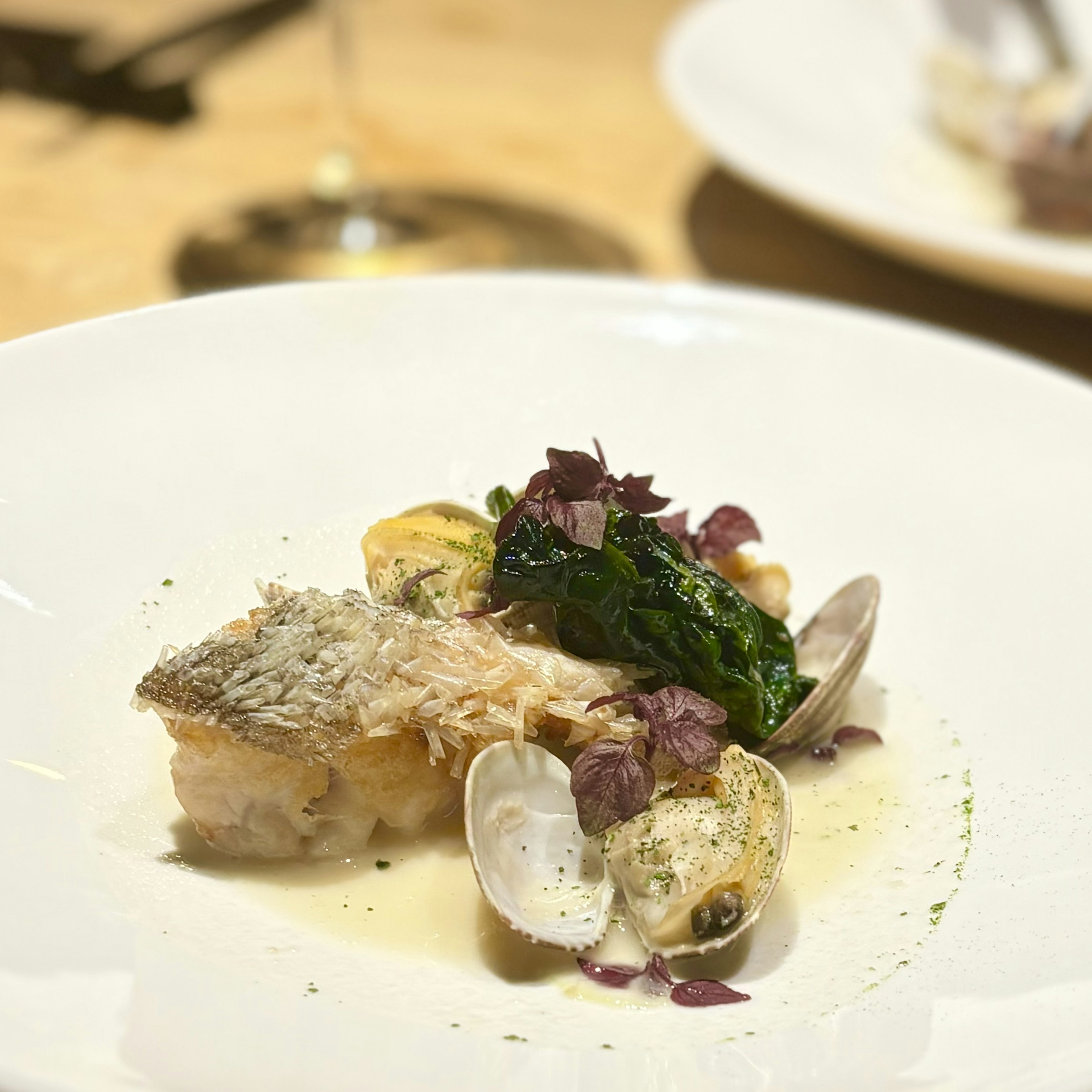 Un plato bellamente presentado con pescado a la parrilla y almejas decorado con espinacas frescas y hierbas moradas