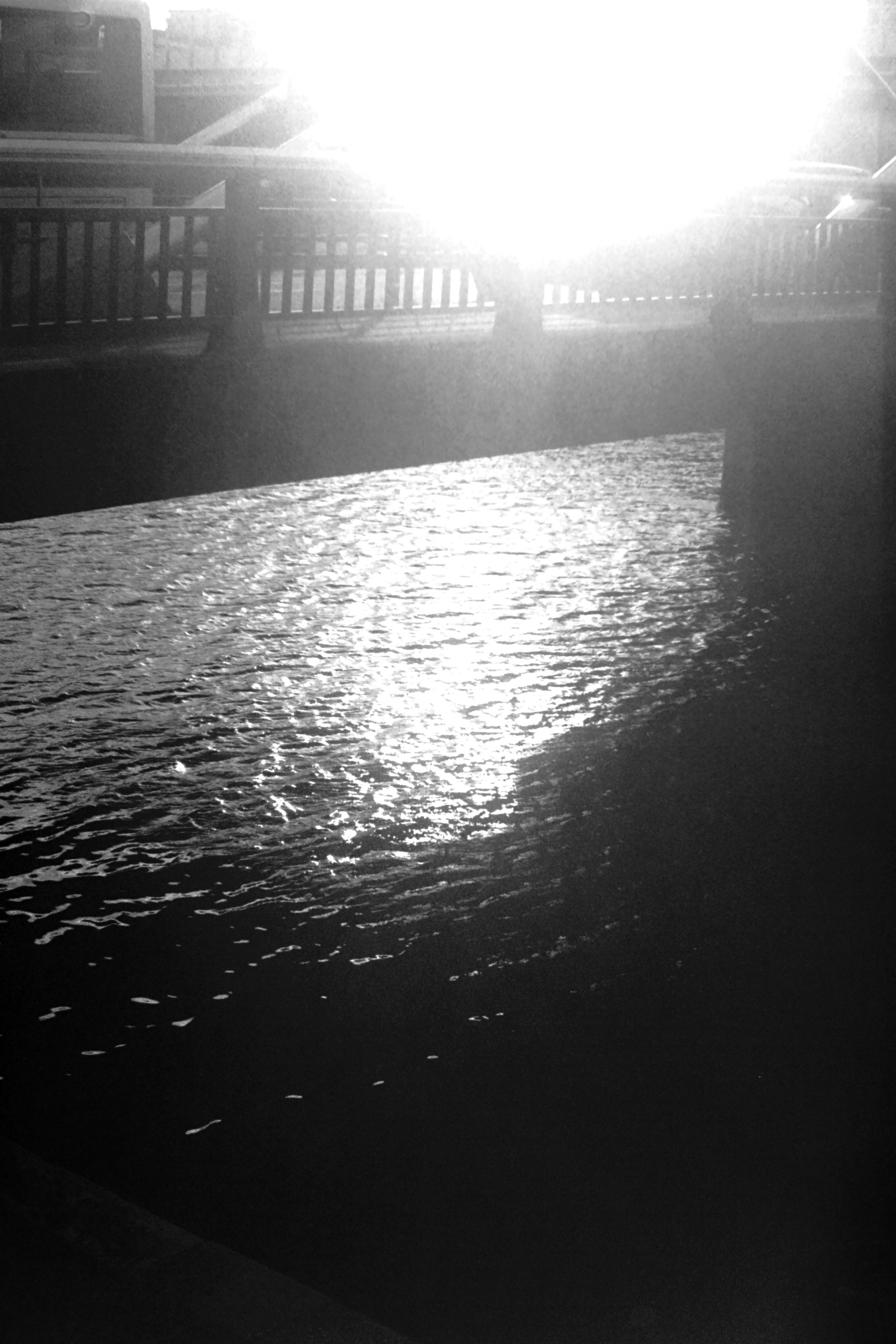 Black and white image of water reflecting light with a bridge silhouette