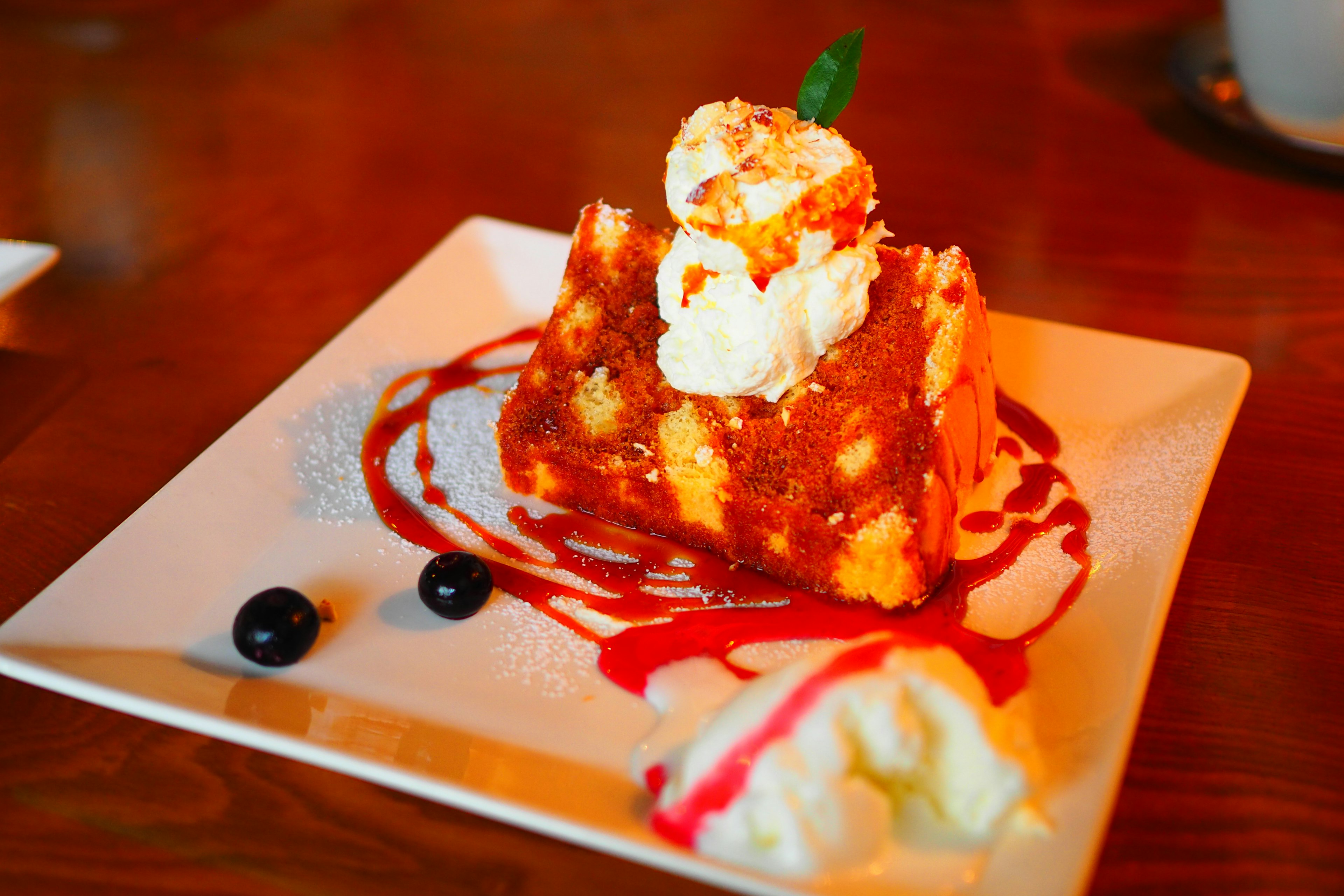 A slice of cake topped with whipped cream on a decorative plate with berry sauce