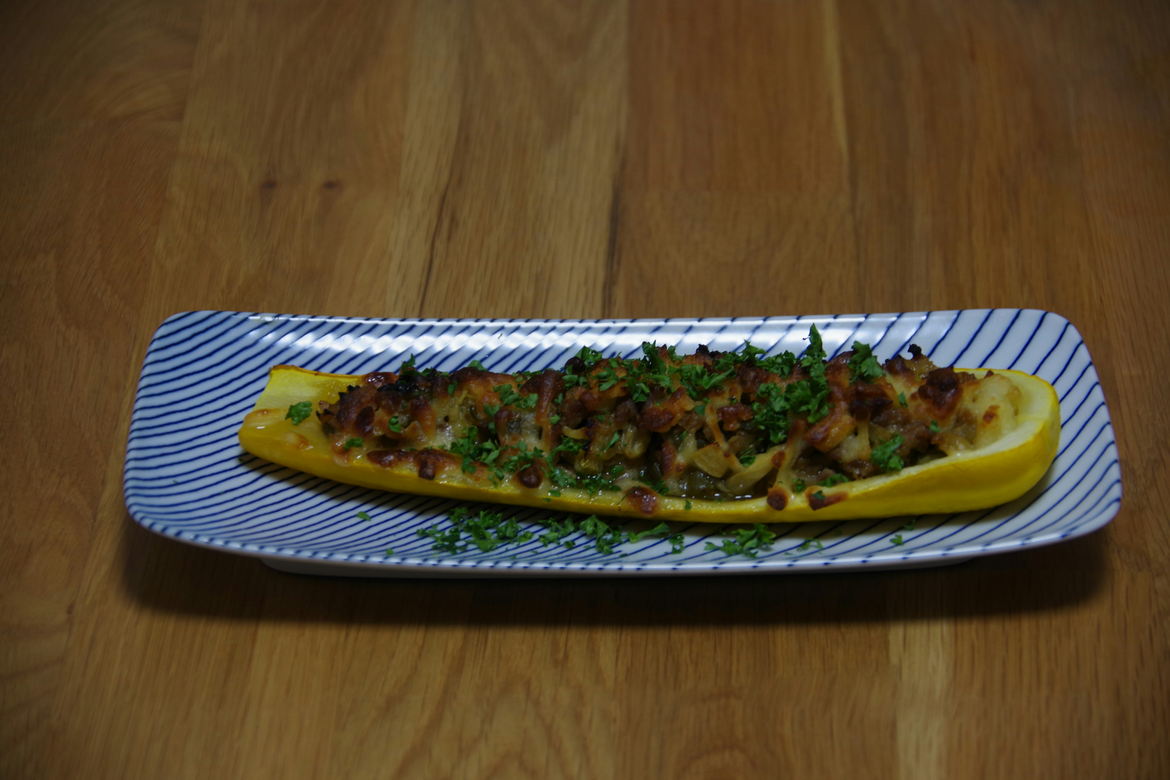 Un plat de courgette cuite présenté sur une assiette rectangulaire longue garni d'herbes