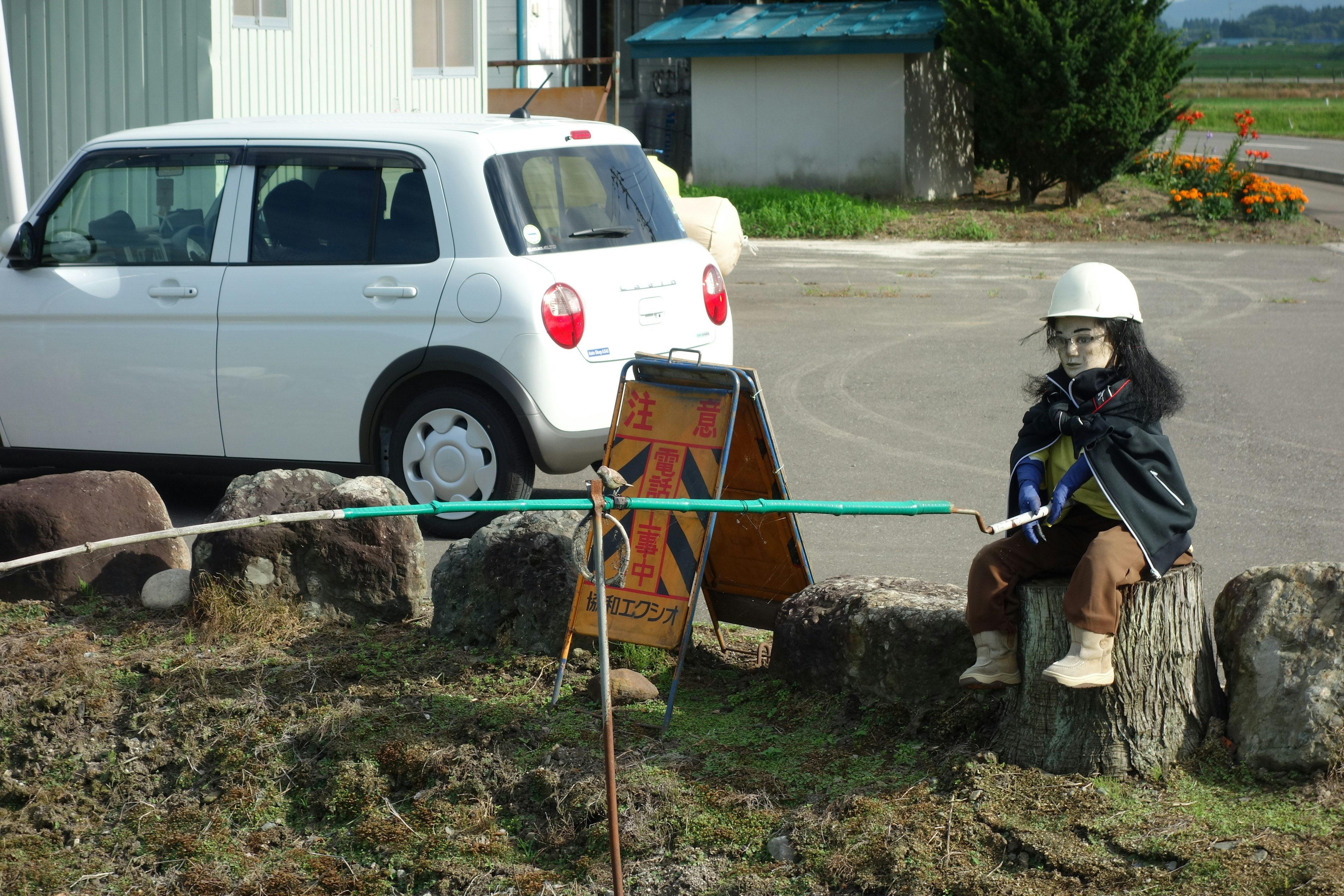 Boneka berpakaian kerja duduk di samping mobil putih dengan latar belakang pedesaan