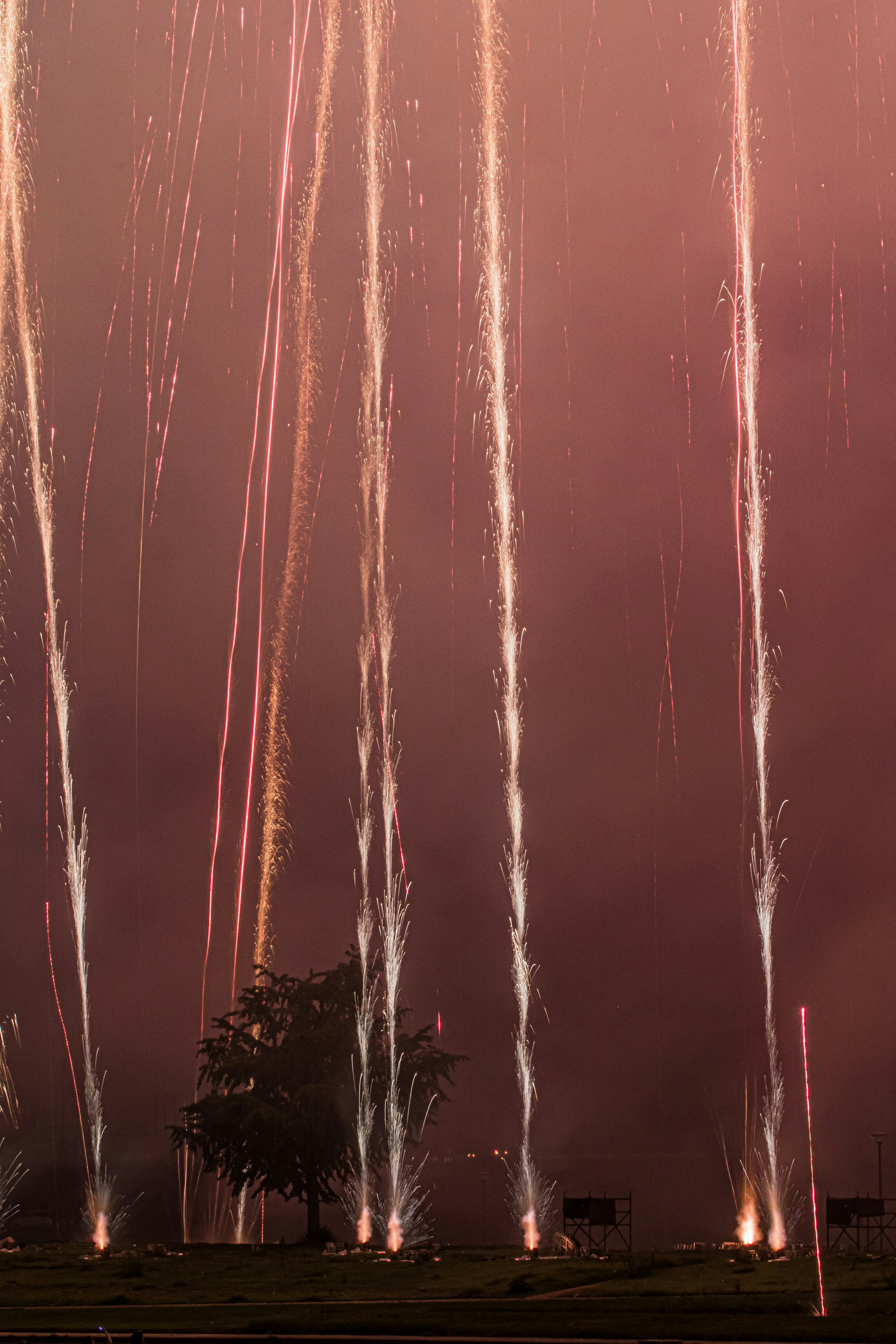 Fuegos artificiales disparándose hacia el cielo nocturno con nubes oscuras de fondo