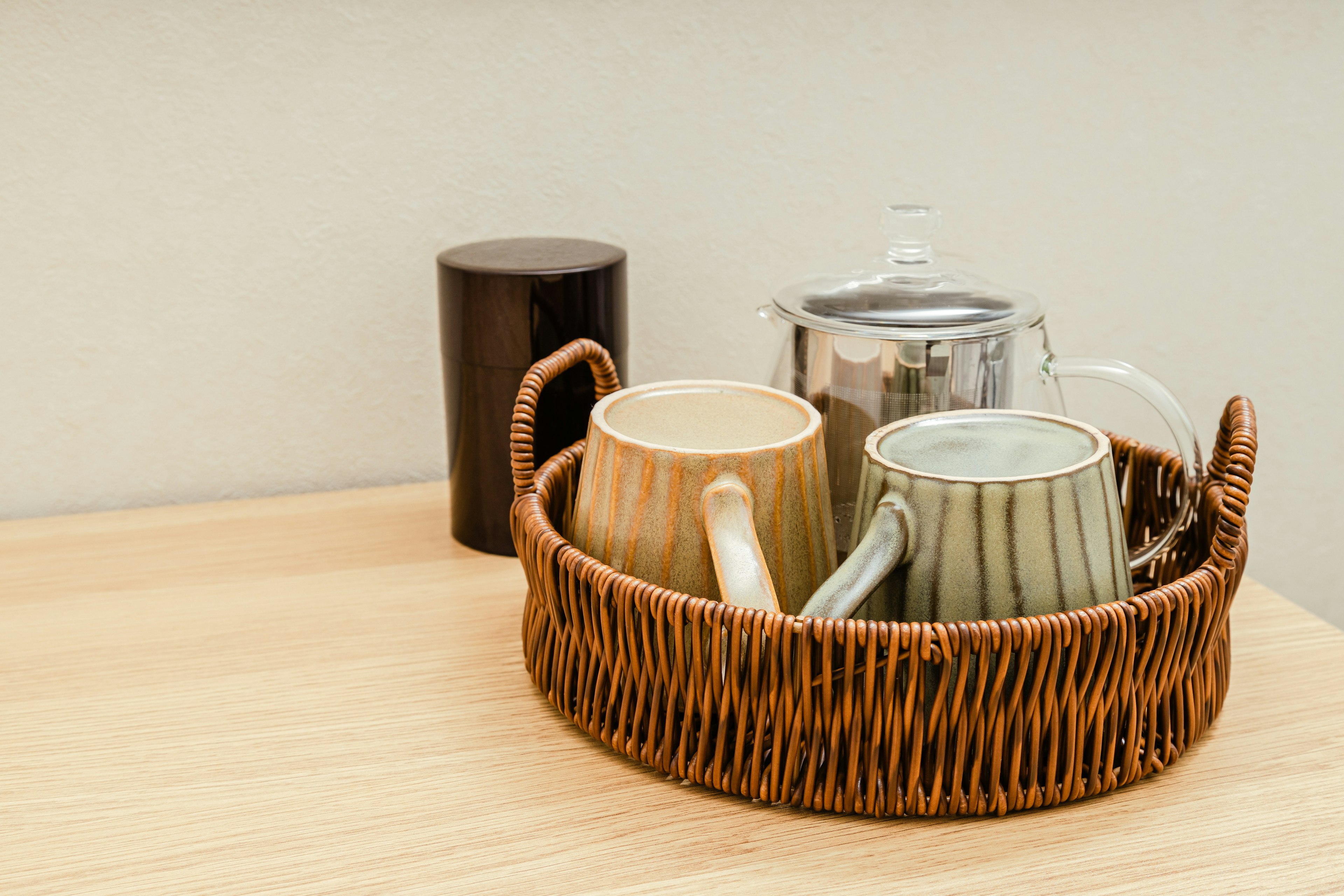 Colorful mugs and a teapot in a brown basket on a wooden table