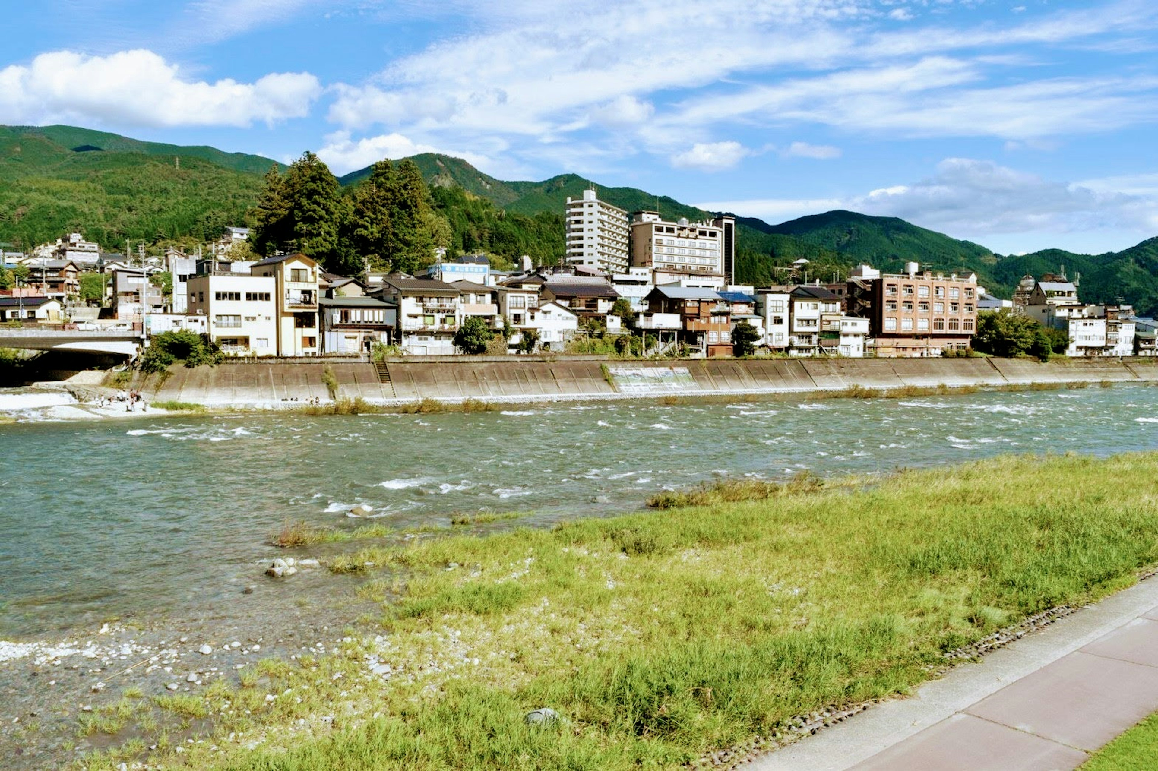 Scenic view of buildings along the river with green mountains in the background