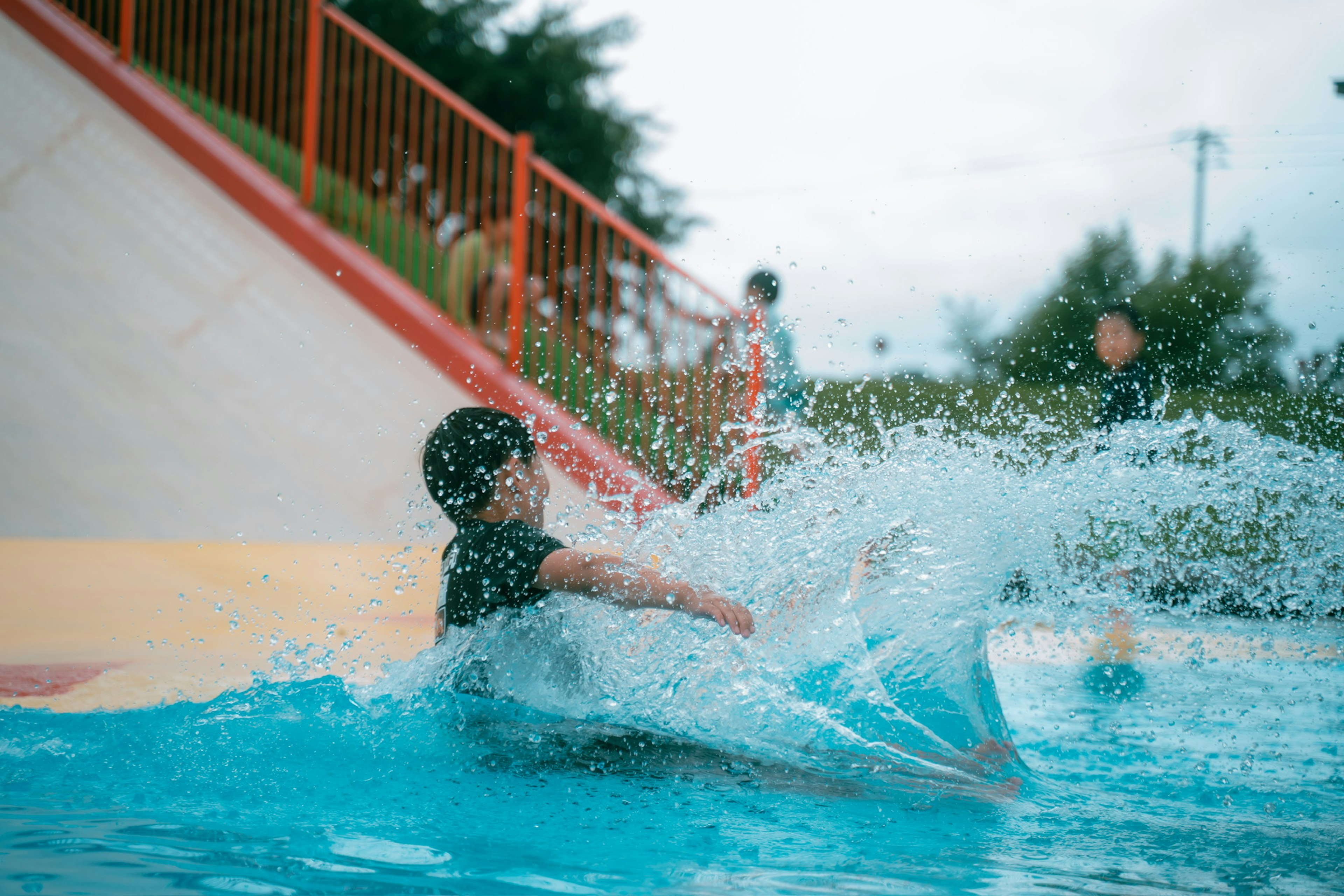 Kind spritzt Wasser, während es von einer Wasserrutsche in einem Spielplatz rutscht