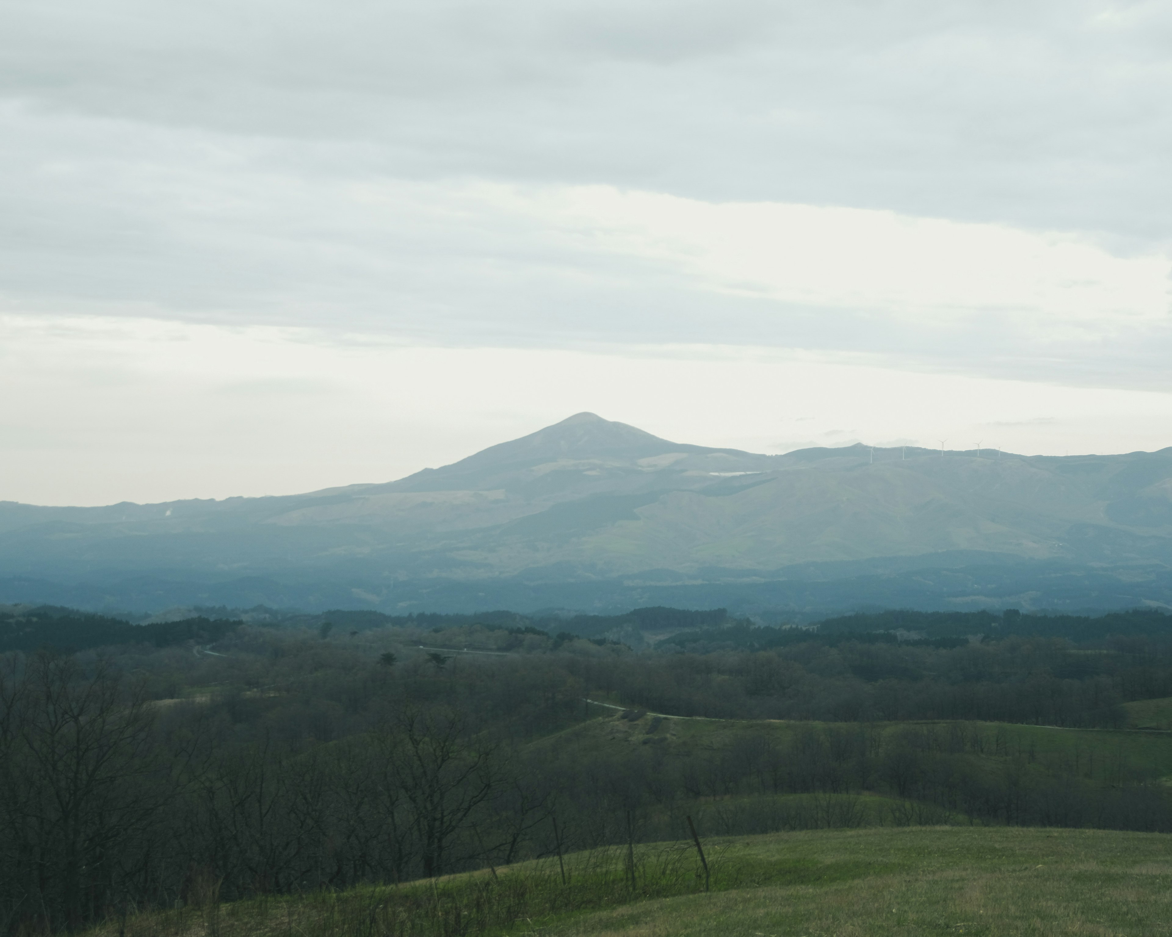 Un paesaggio con colline verdi e montagne lontane sotto un cielo nuvoloso