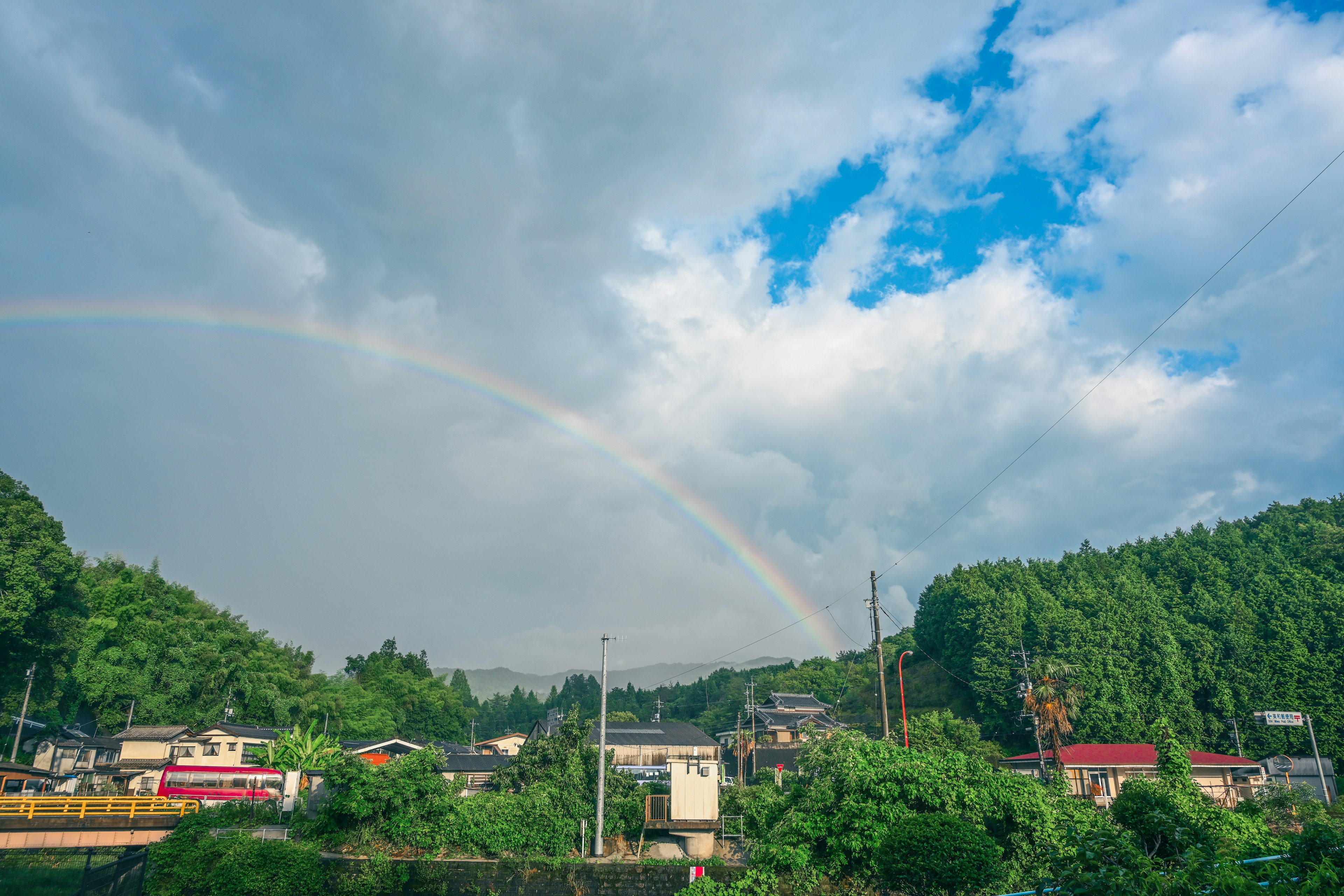 Ein Regenbogen spannt sich zwischen blauen Himmel und Wolken über grünen Hügeln und Häusern