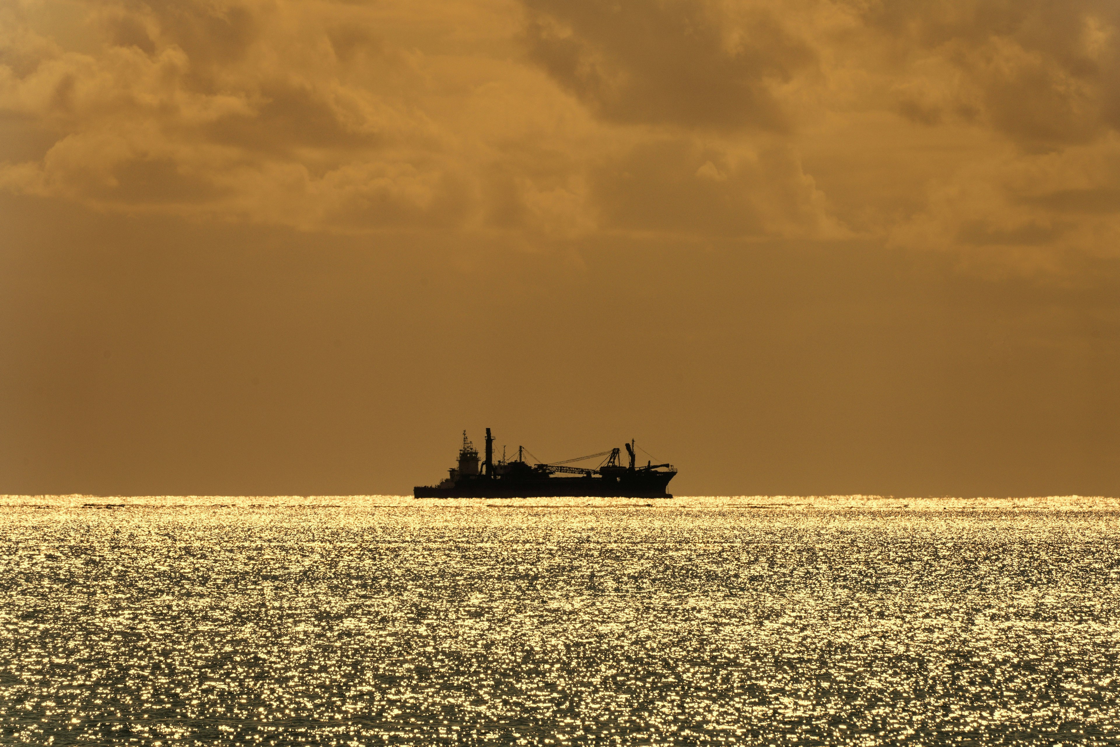 Ship silhouetted against a golden sea and cloudy sky