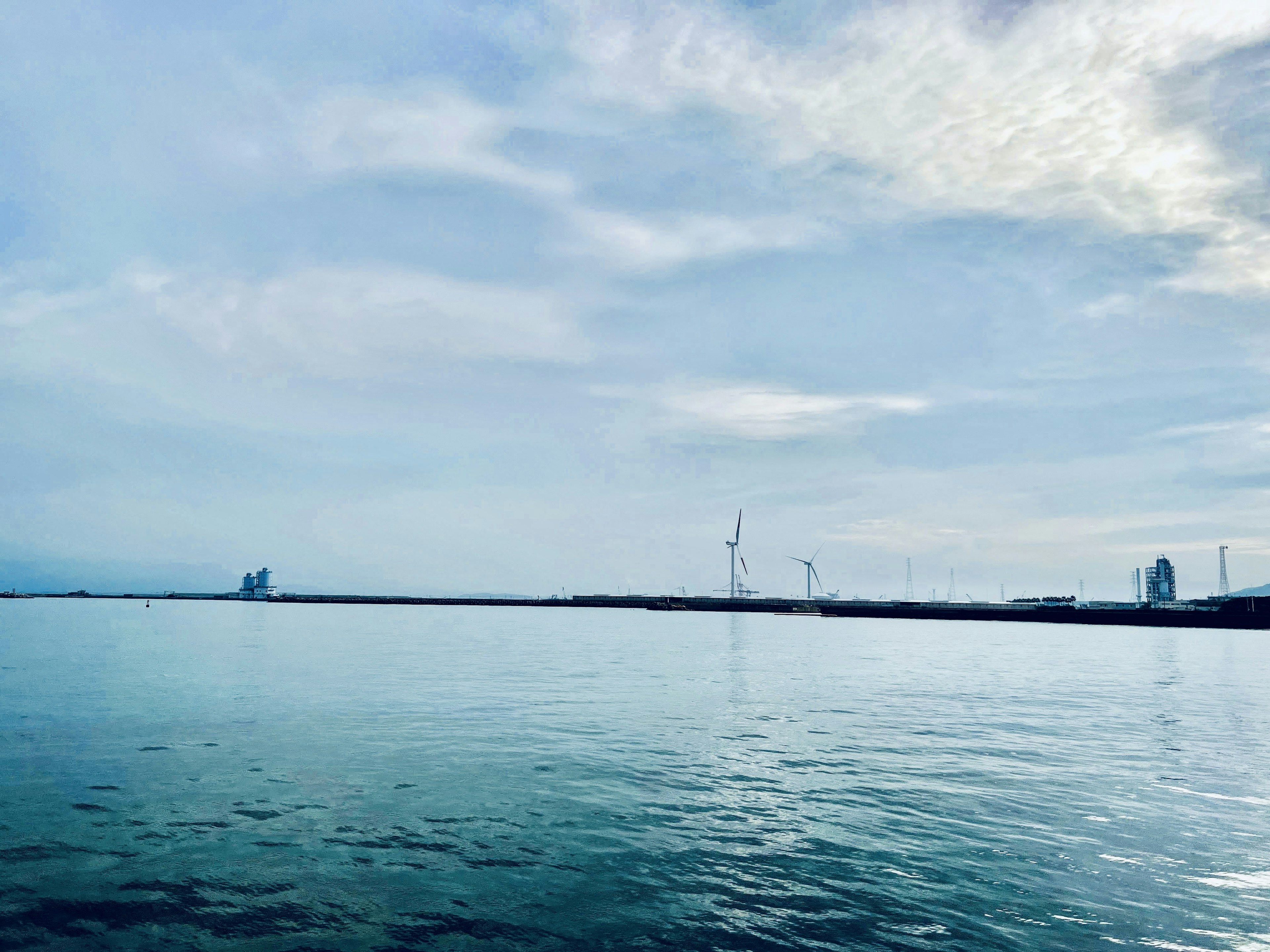 Vista panoramica di mare calmo e cielo blu con turbine eoliche all'orizzonte