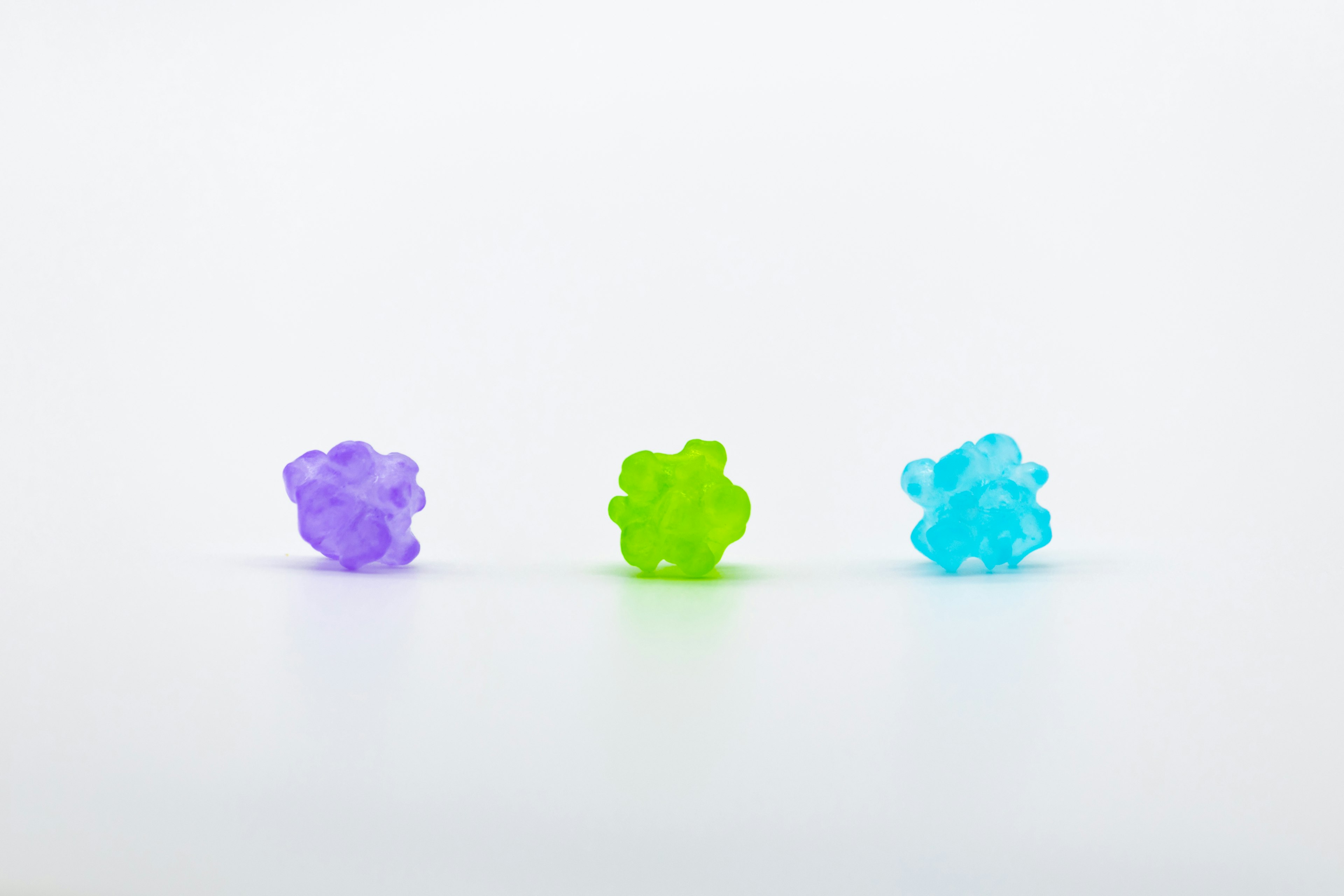 Purple green and blue gummy bears arranged on a white background