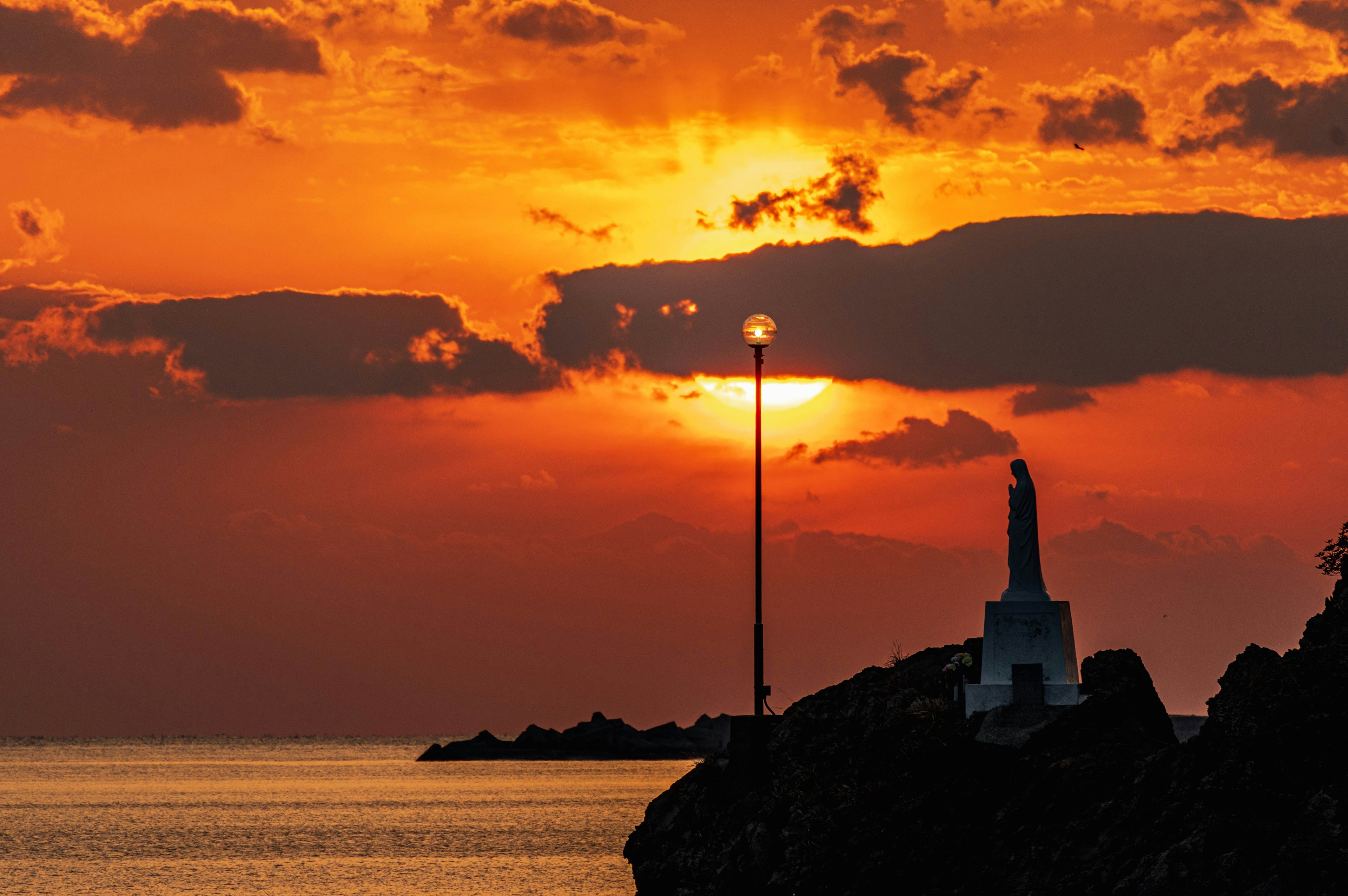 Monument silhouetted against a vibrant sunset over the sea