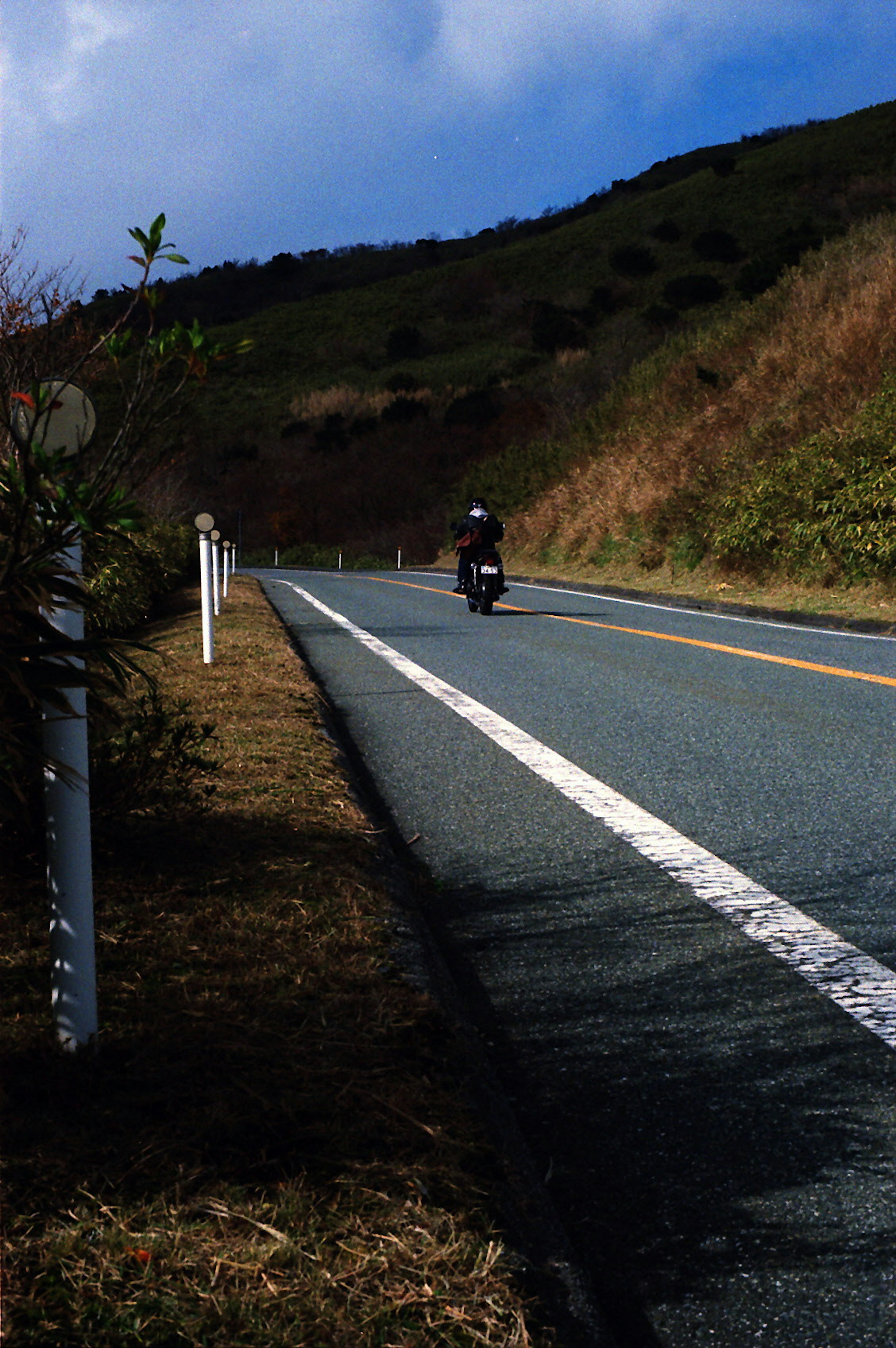 摩托車在綠色山丘旁的道路上行駛