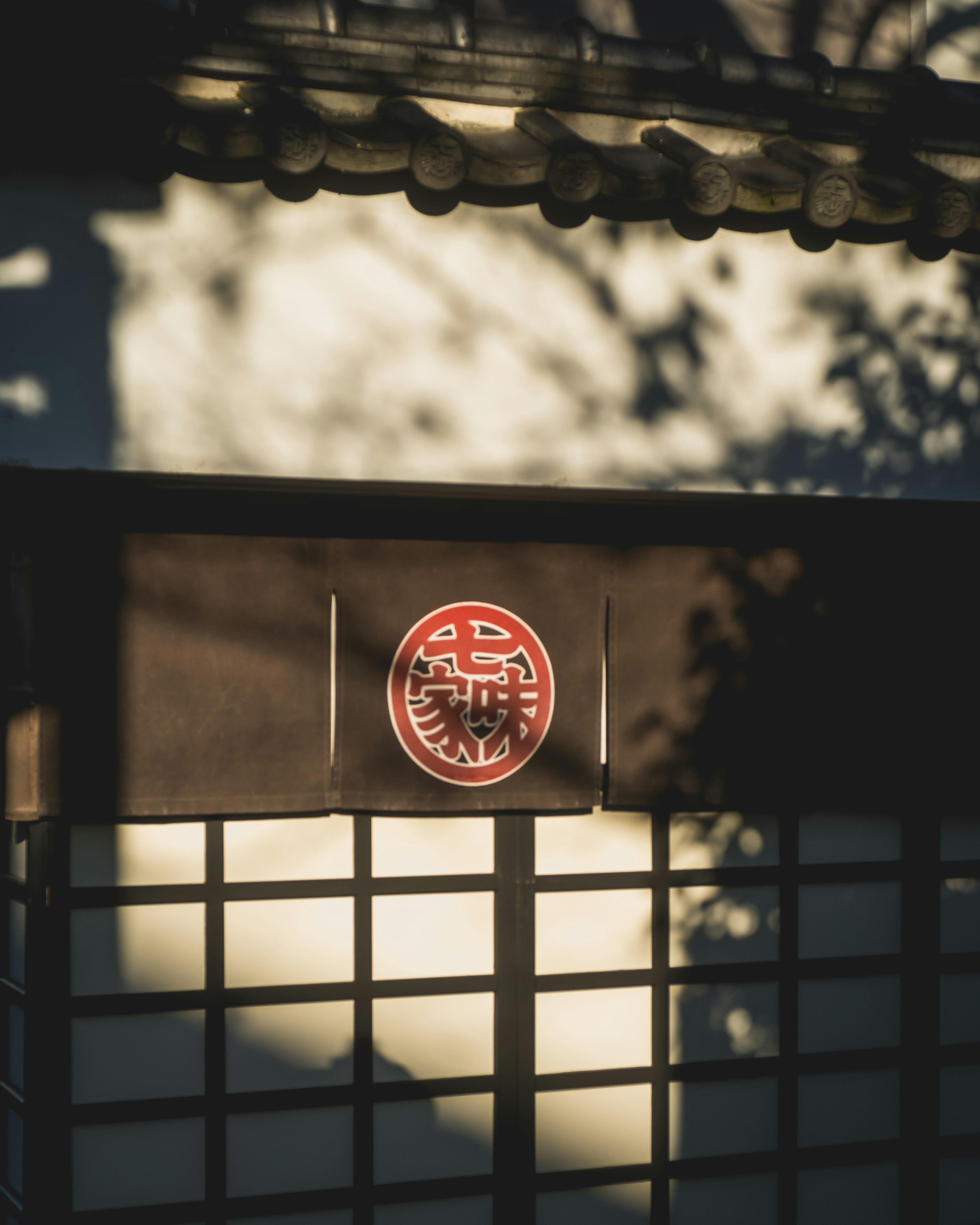 Äußere eines traditionellen japanischen Gebäudes mit Schatten und einem roten Emblem