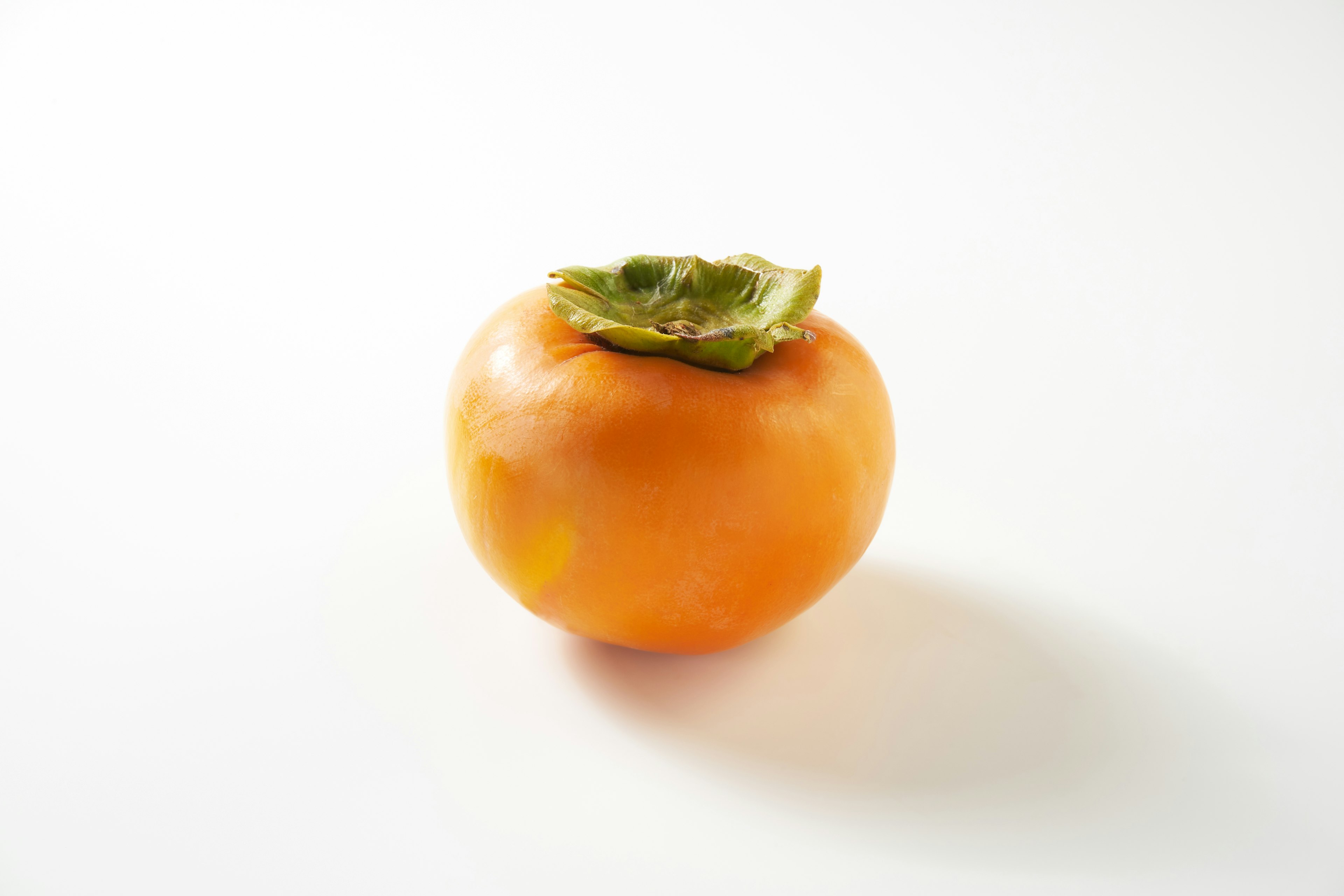 Eine orangefarbene Persimone mit grünen Blättern auf einem weißen Hintergrund