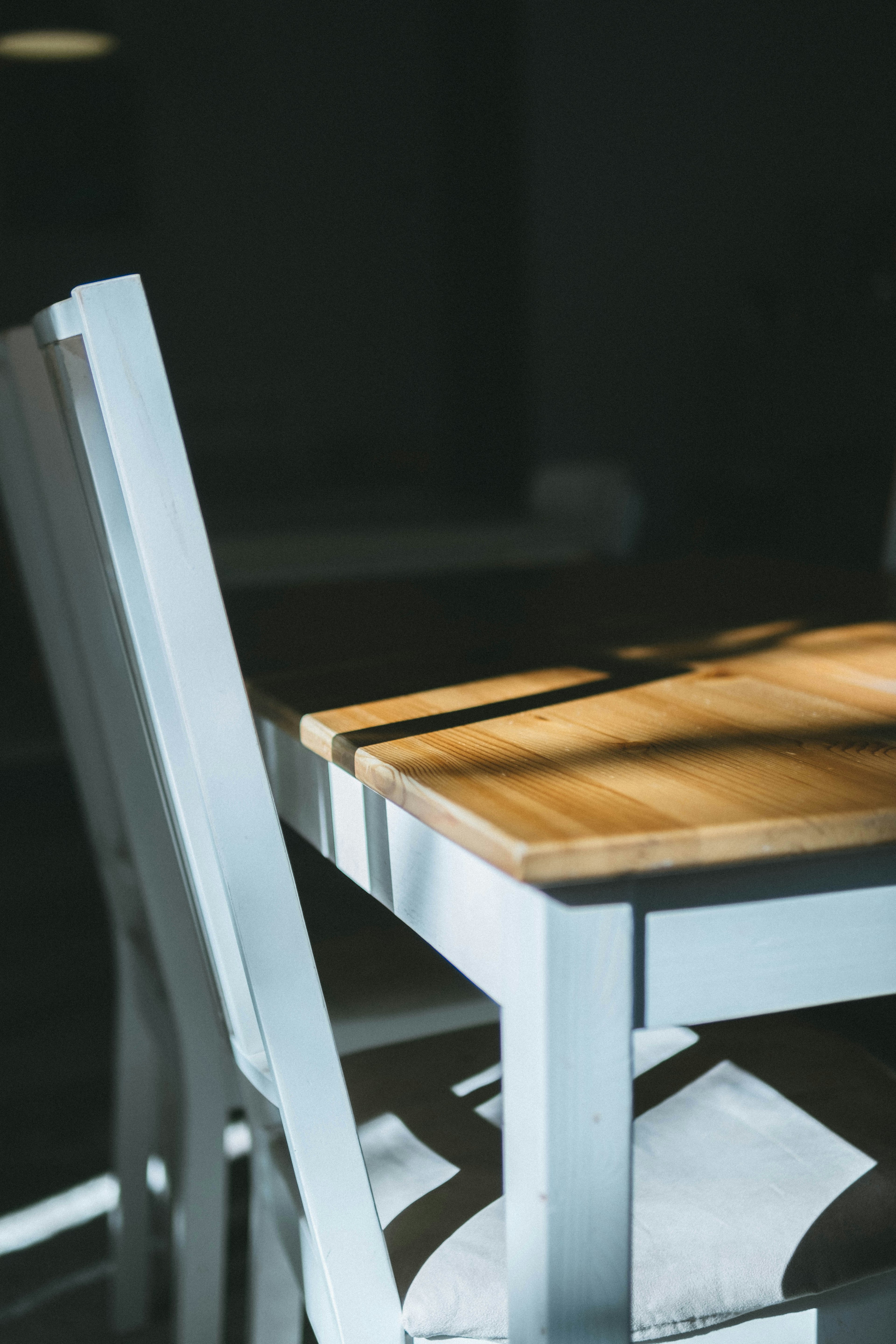 Primo piano di una sedia bianca e di un tavolo in legno in una stanza poco illuminata