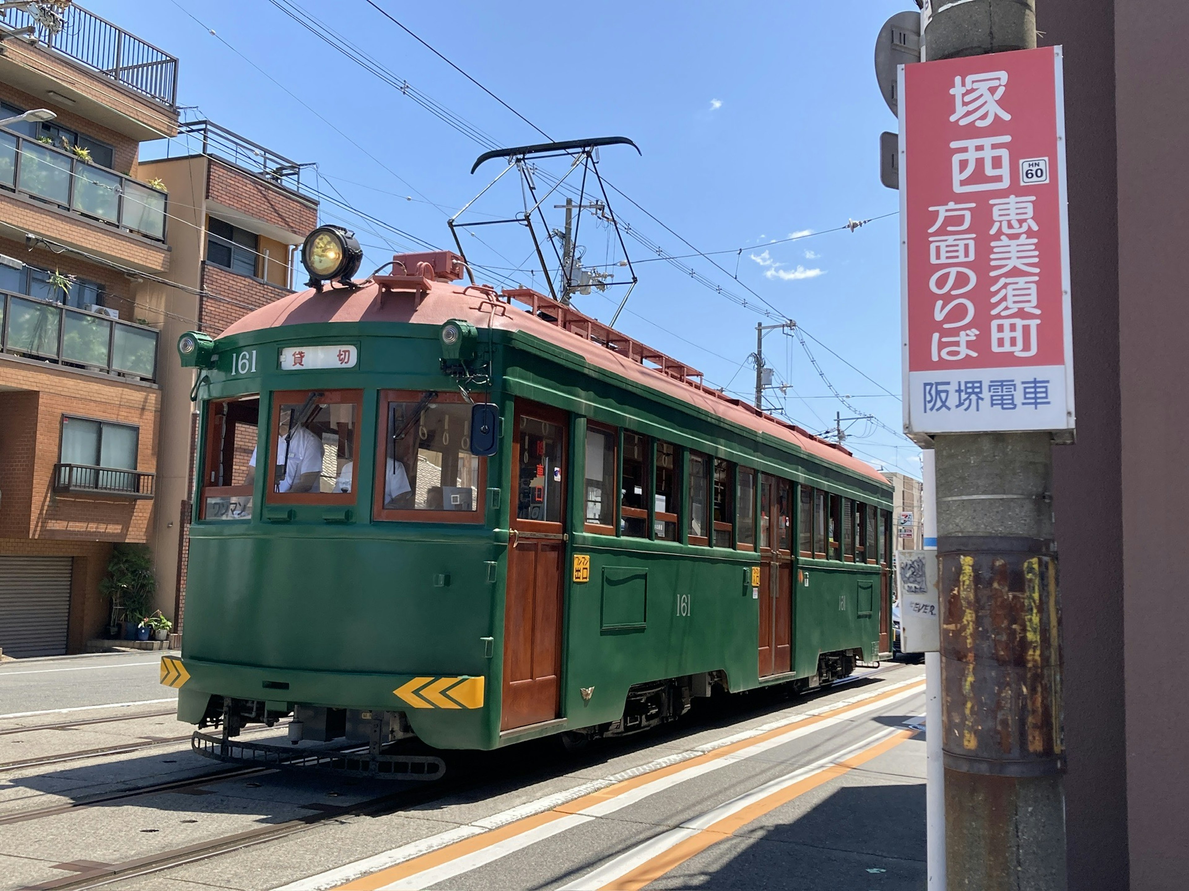 A vintage green streetcar passing by a station in a sunny urban setting