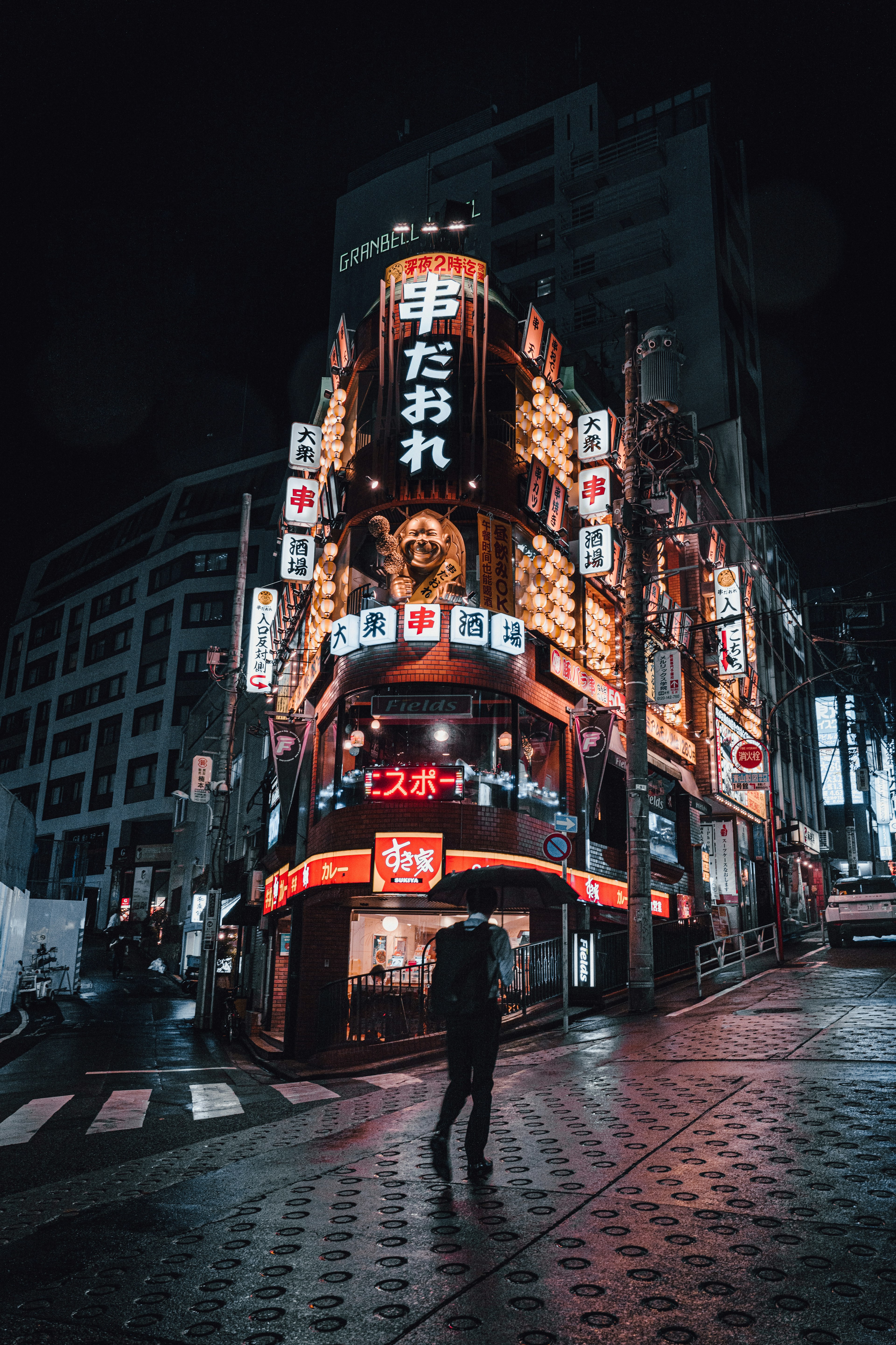 Un peatón pasando por un izakaya iluminado con neón de noche