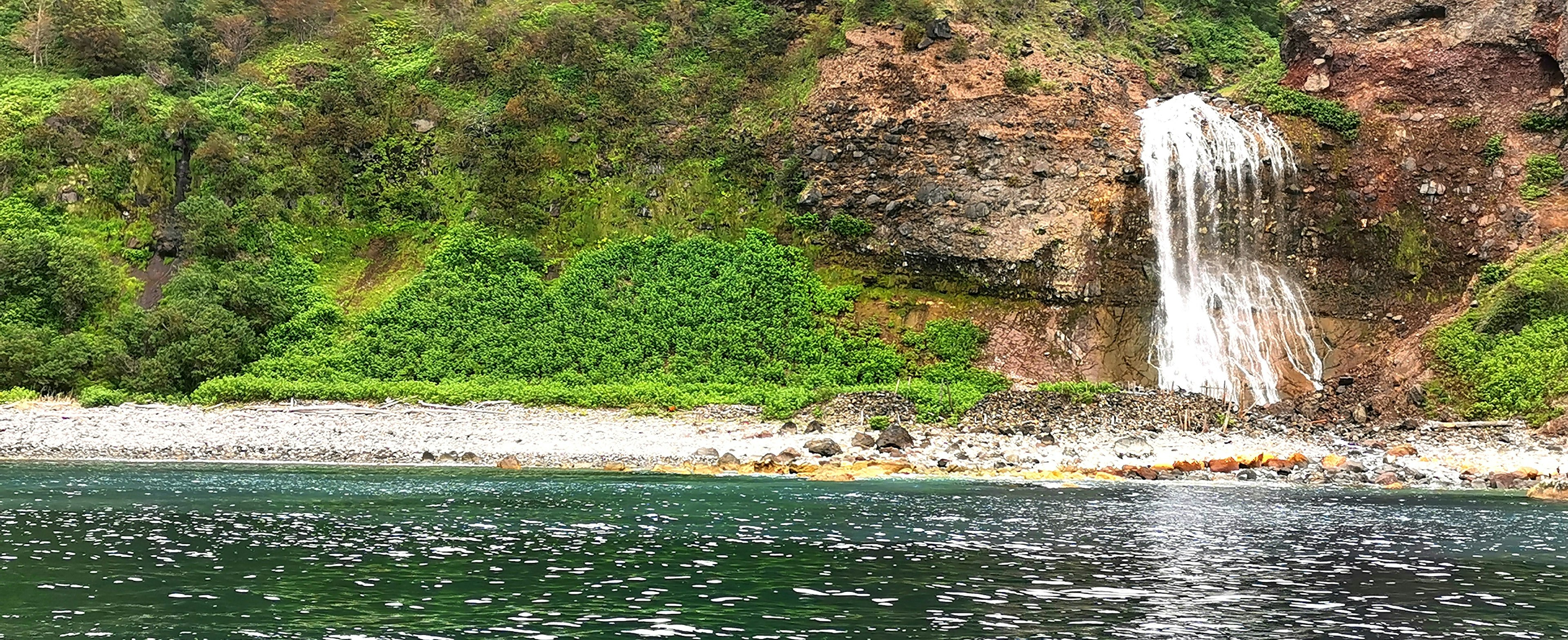 Vista escénica de un lago con colinas verdes y una cascada