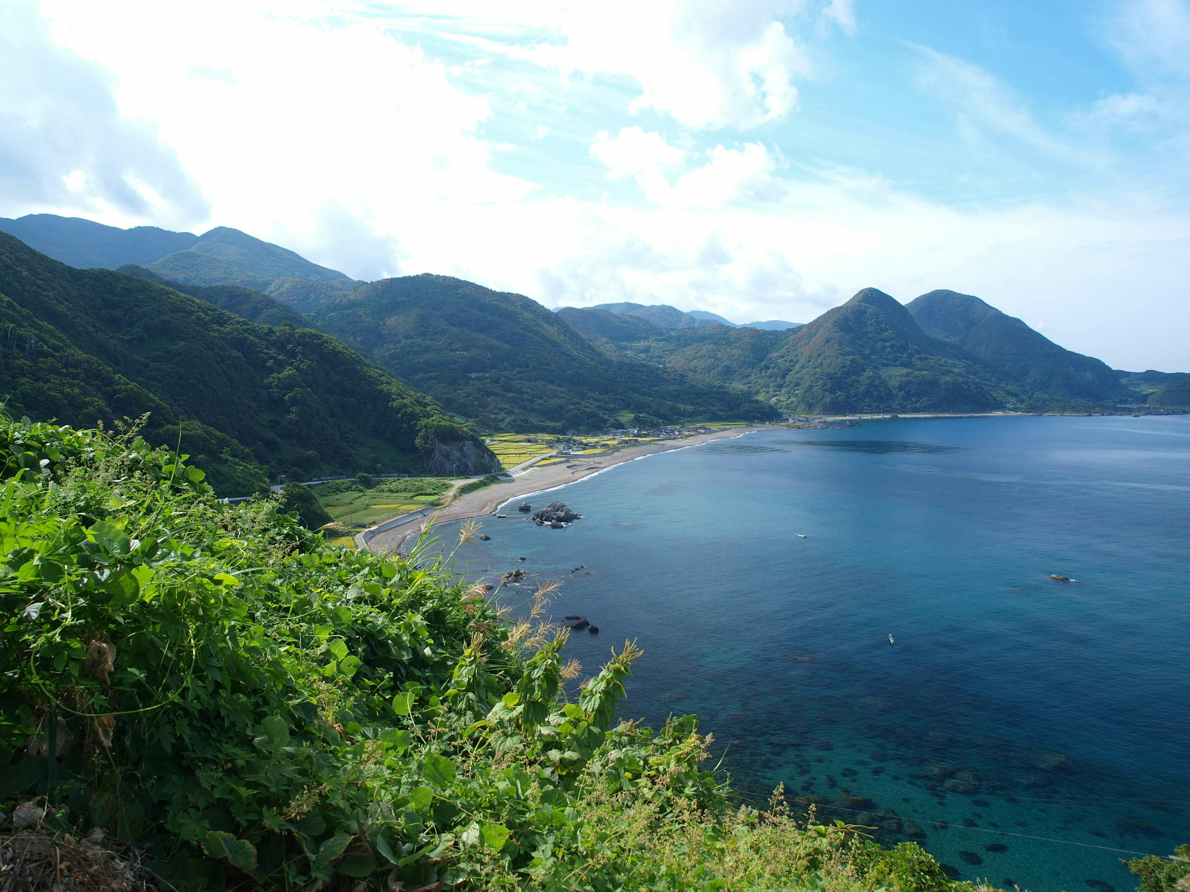 Costa panoramica con montagne vegetazione lussureggiante in primo piano mare blu e cielo