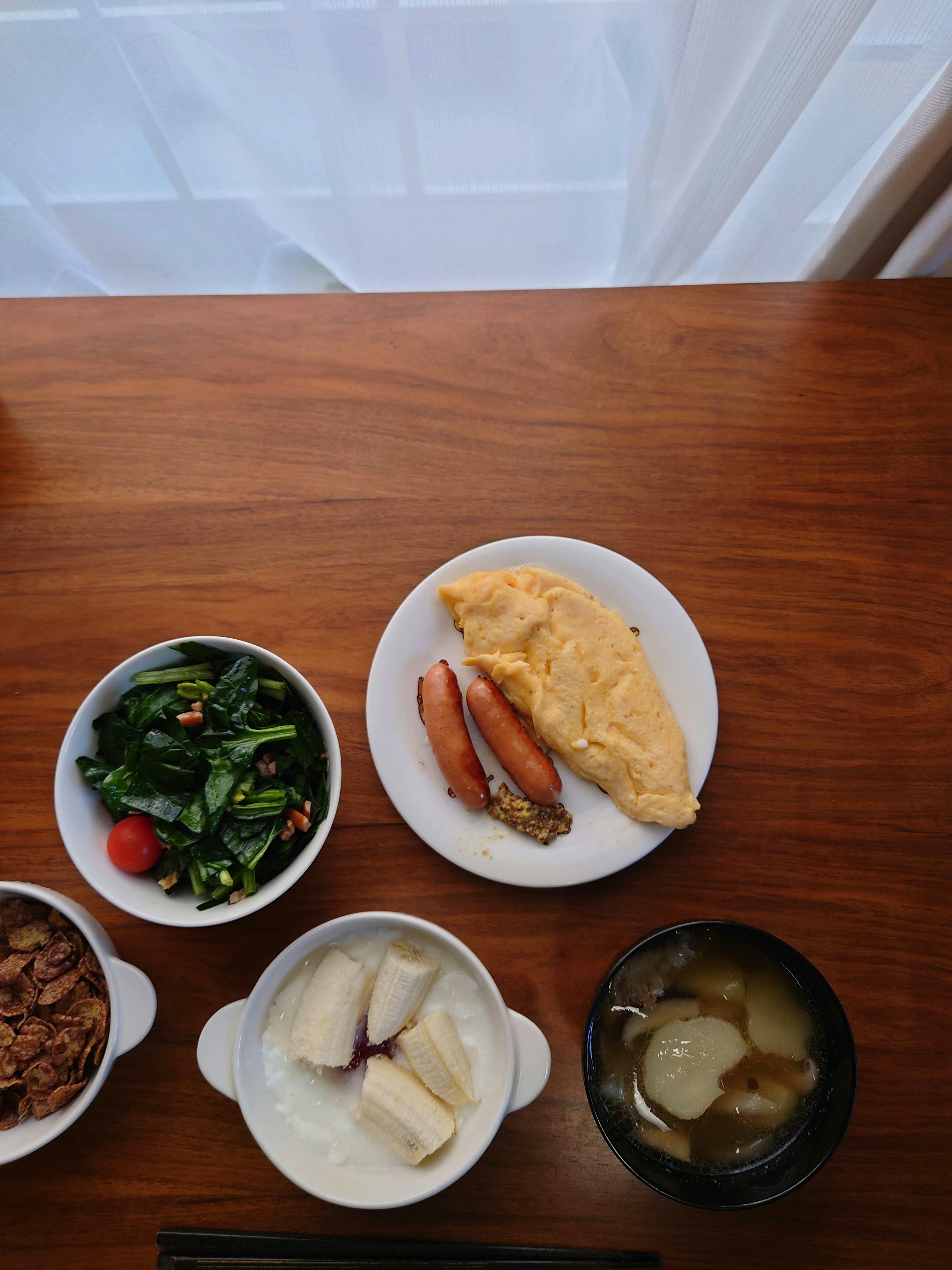 Repas de petit-déjeuner sur une table avec une omelette des saucisses une salade et de la soupe miso