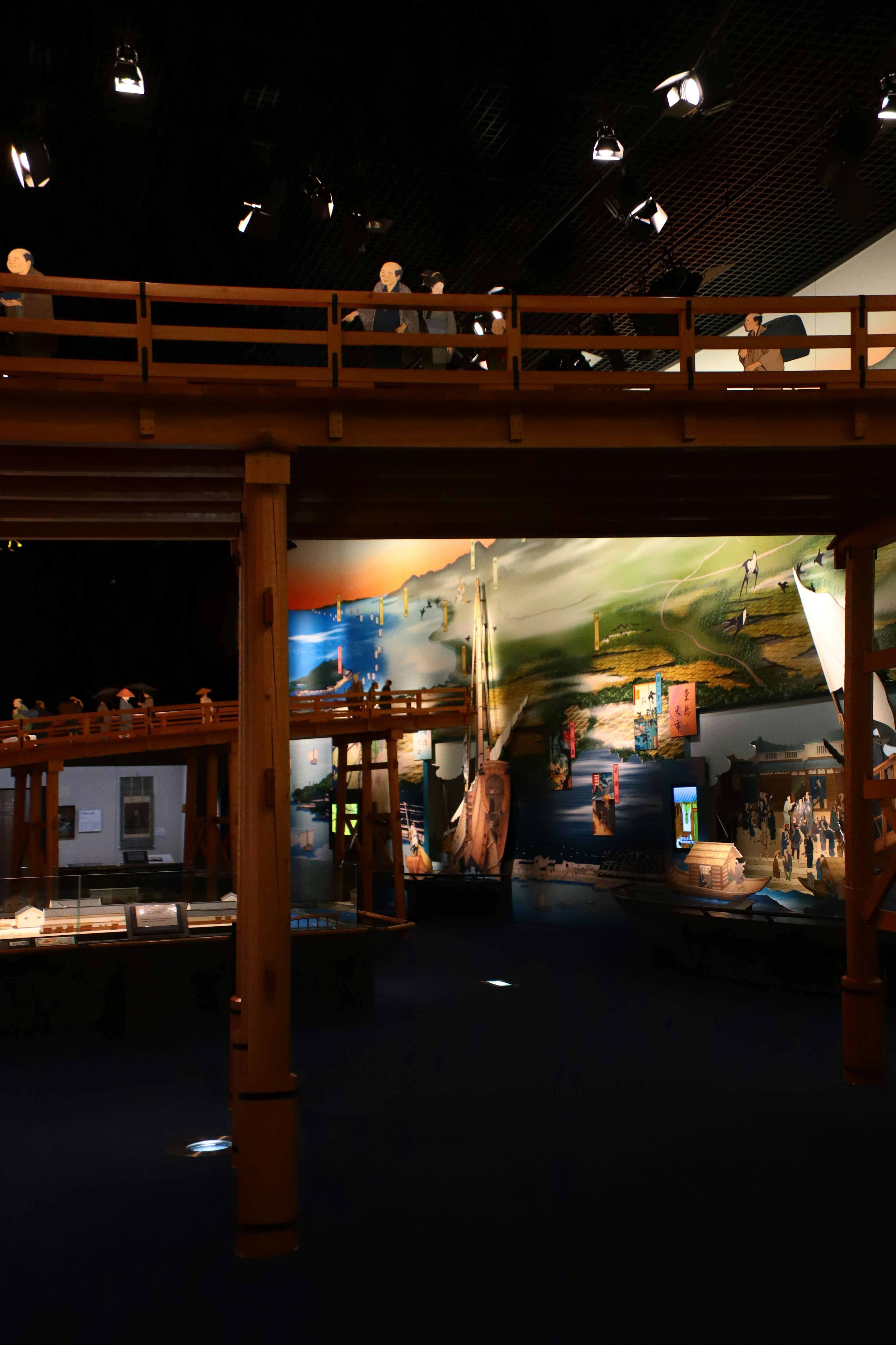 Vista interior de un espacio de exhibición con un puente de madera y murales de paisajes