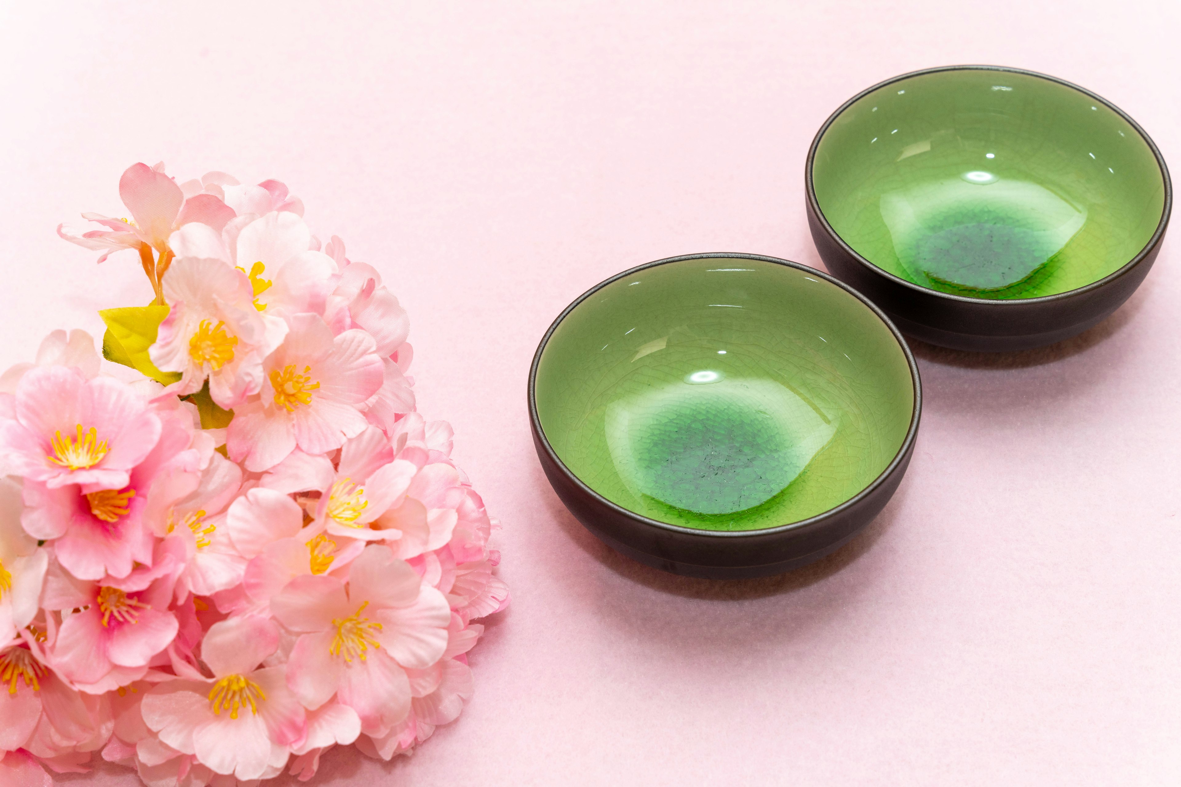 Two green bowls beside pink cherry blossoms on a soft pink background