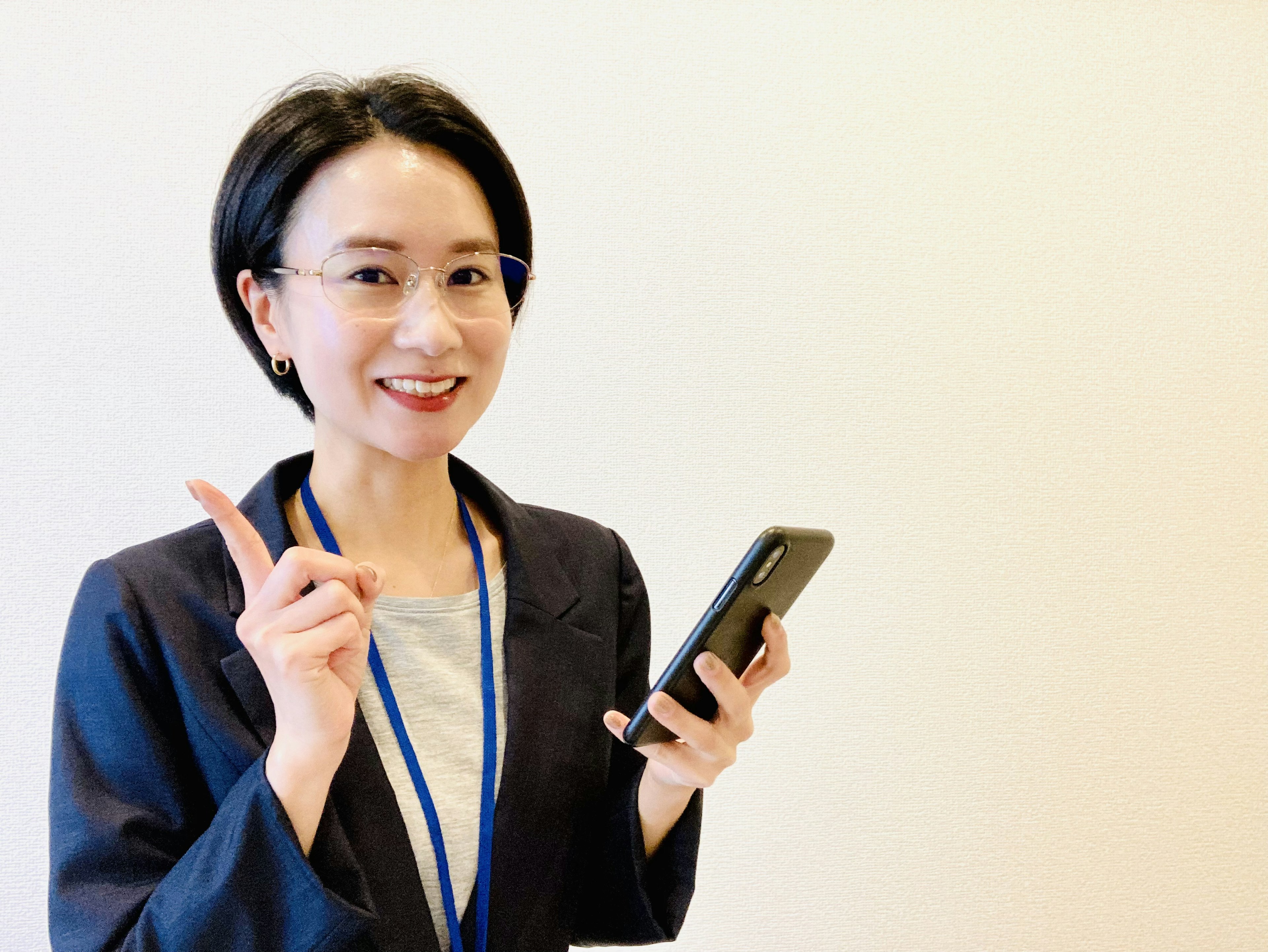 A woman in business attire smiling while holding a smartphone and raising her finger