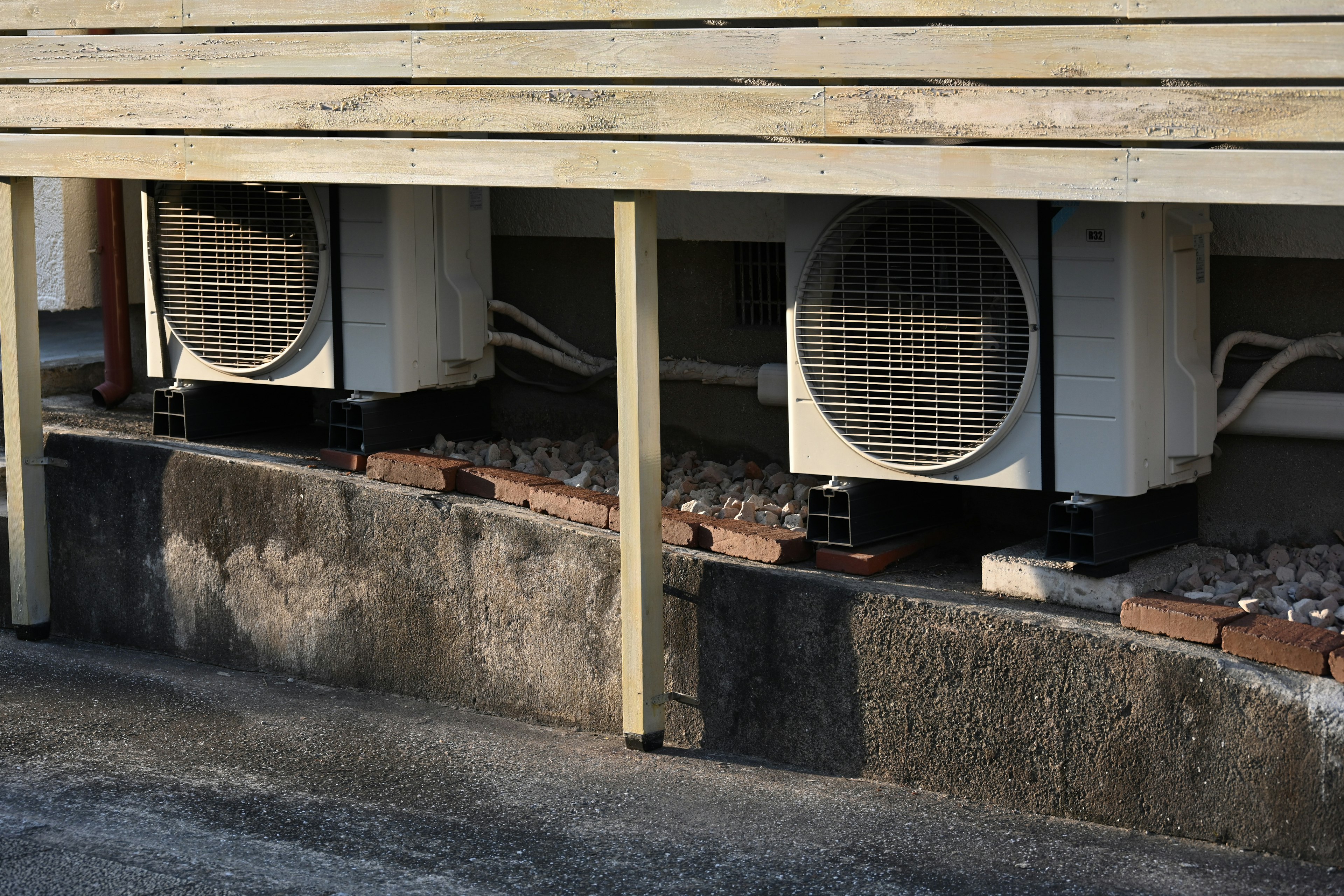 Two outdoor air conditioning units installed beneath a wooden structure