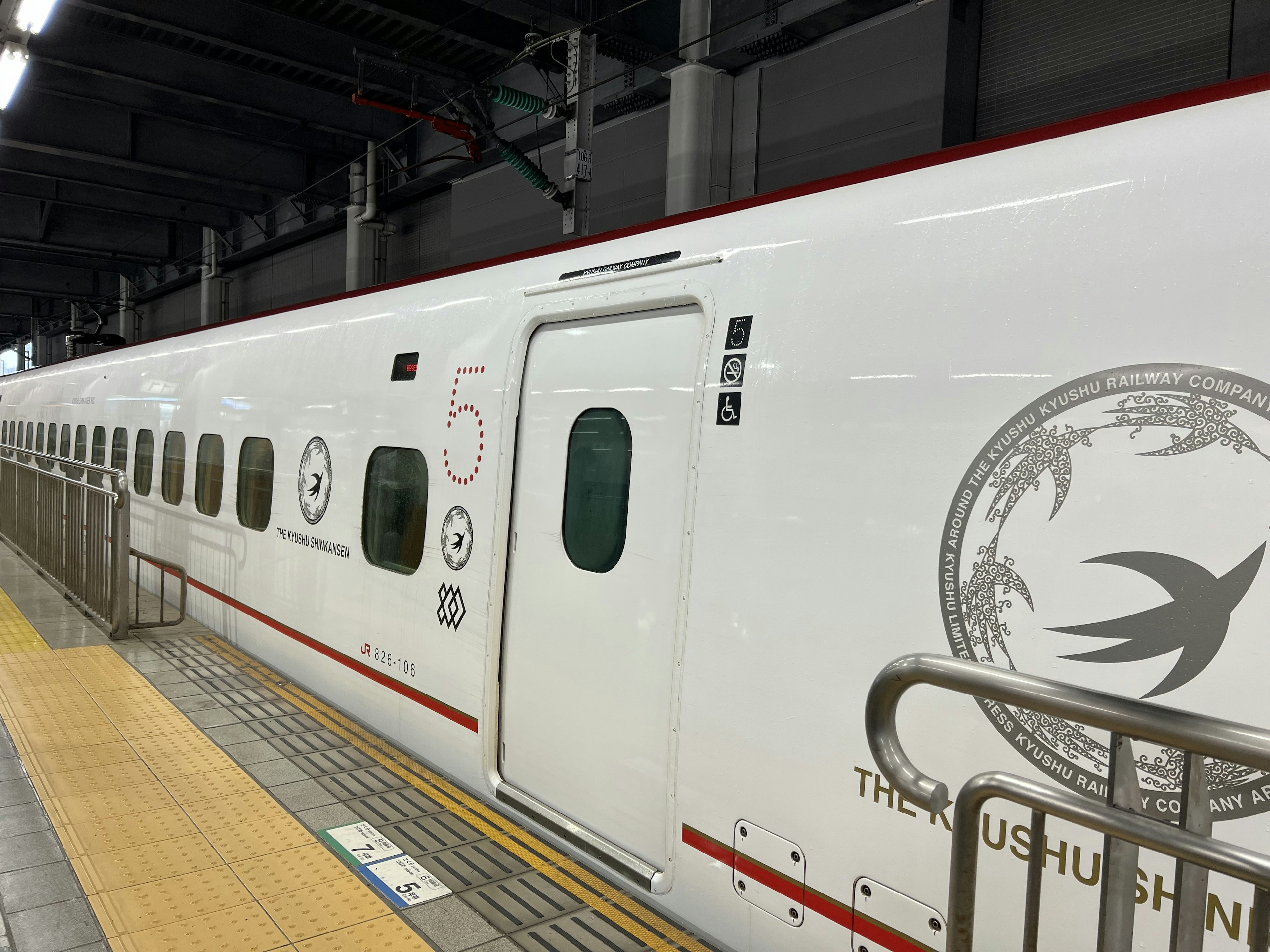 Sebuah kereta Shinkansen putih di stasiun dengan desain burung dan garis merah