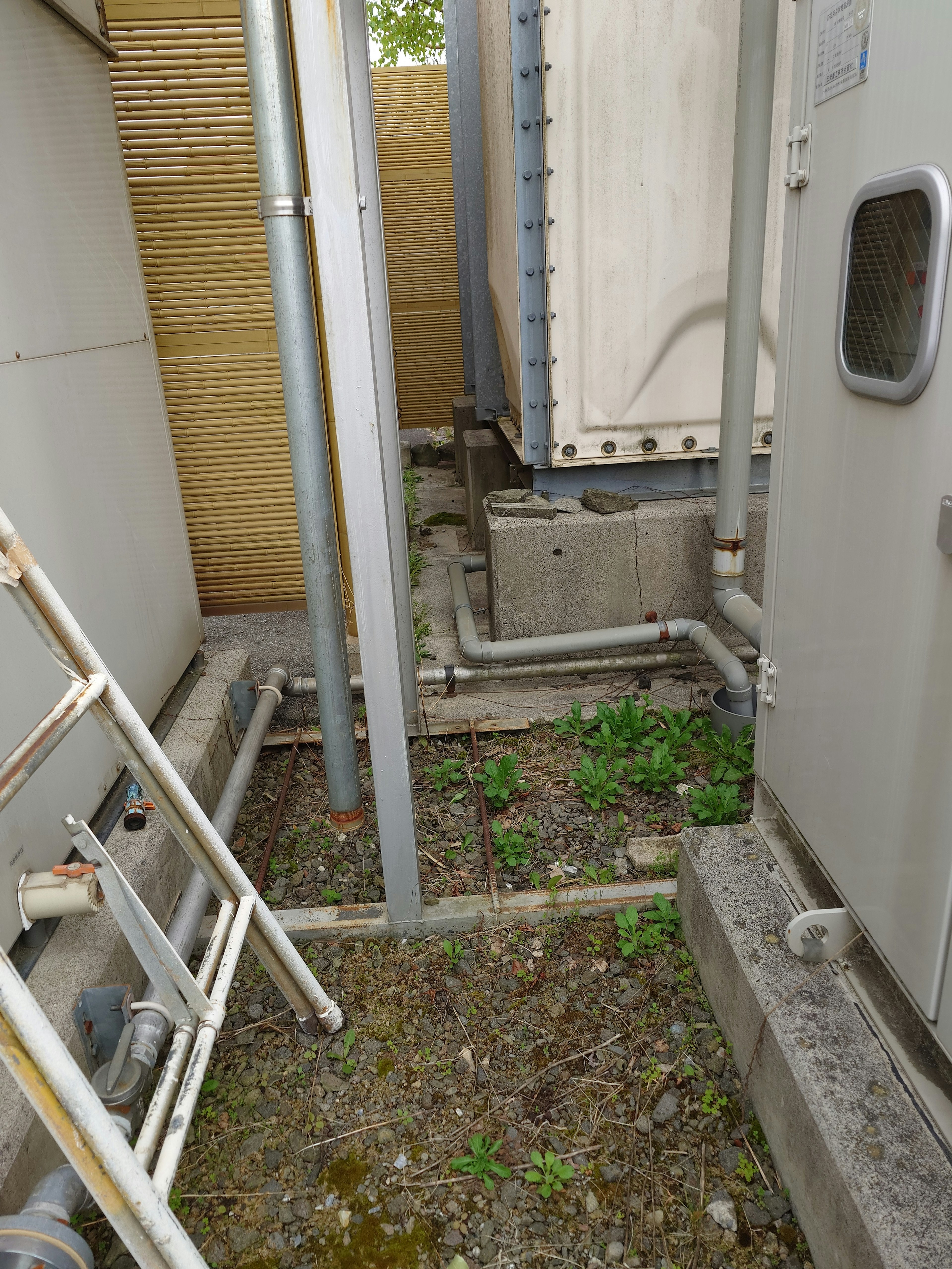 Foto de un espacio estrecho con unidades de refrigeración y tuberías rodeadas de hierba