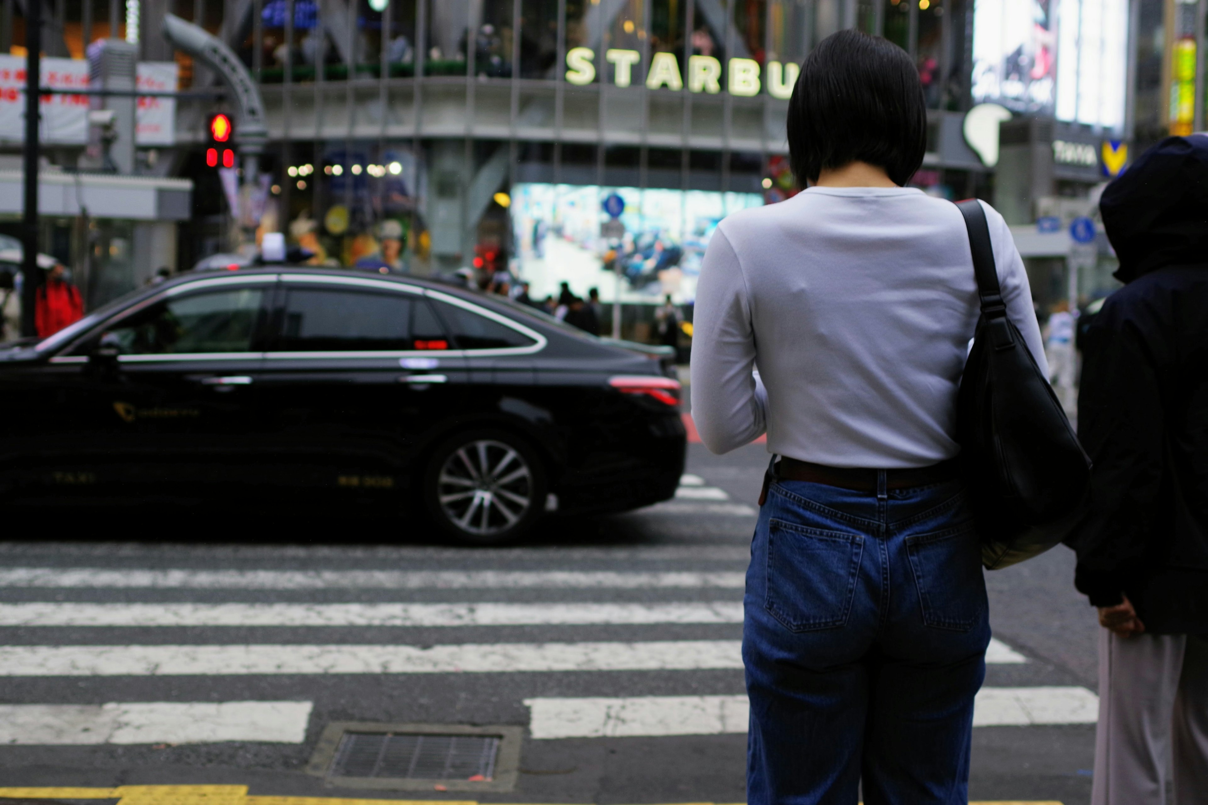 Femme traversant la rue avec une voiture noire en arrière-plan