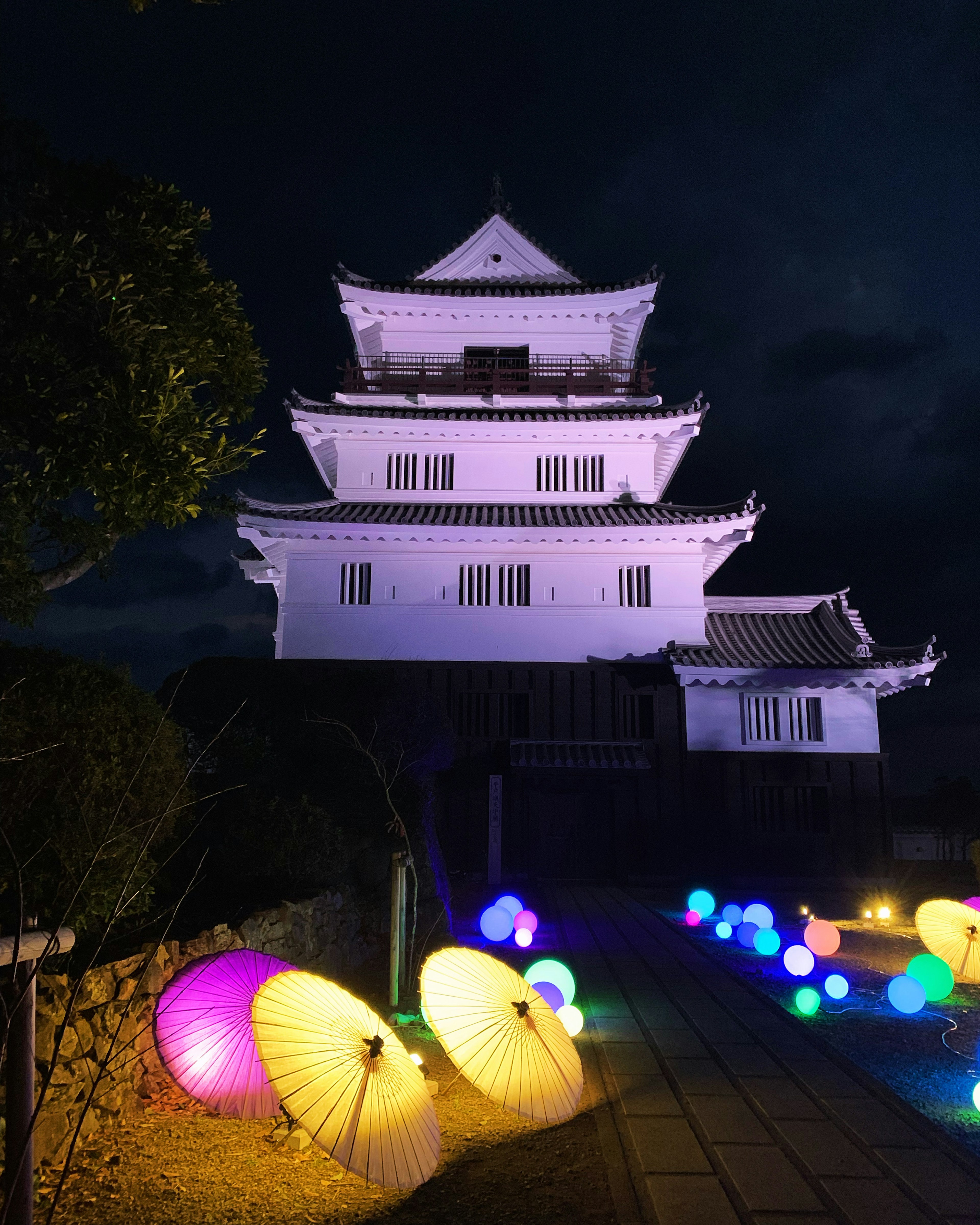 Castillo japonés iluminado por la noche con paraguas coloridos