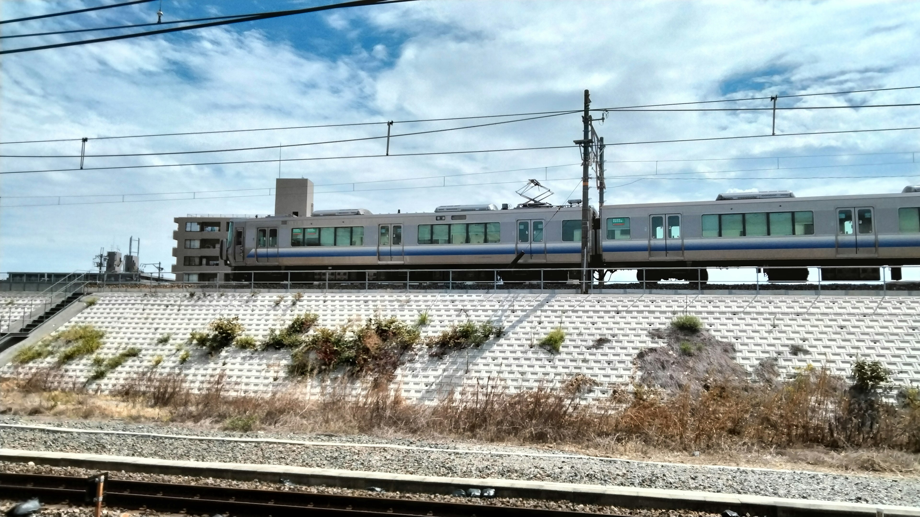 Tren pasando bajo un cielo azul con vías de tren y una pendiente cubierta de hierba