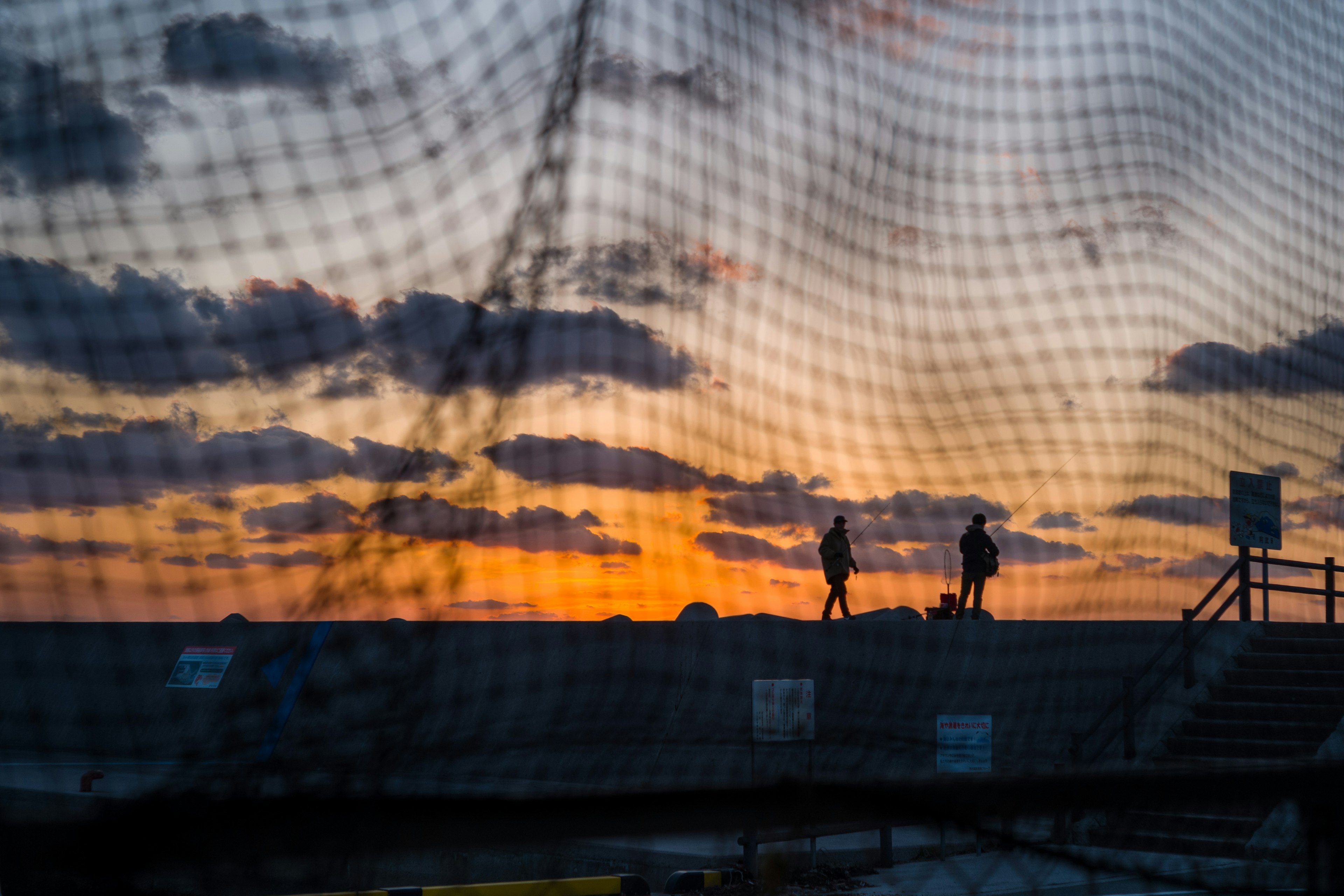 Siluetas de dos personas caminando al atardecer con un fondo de red