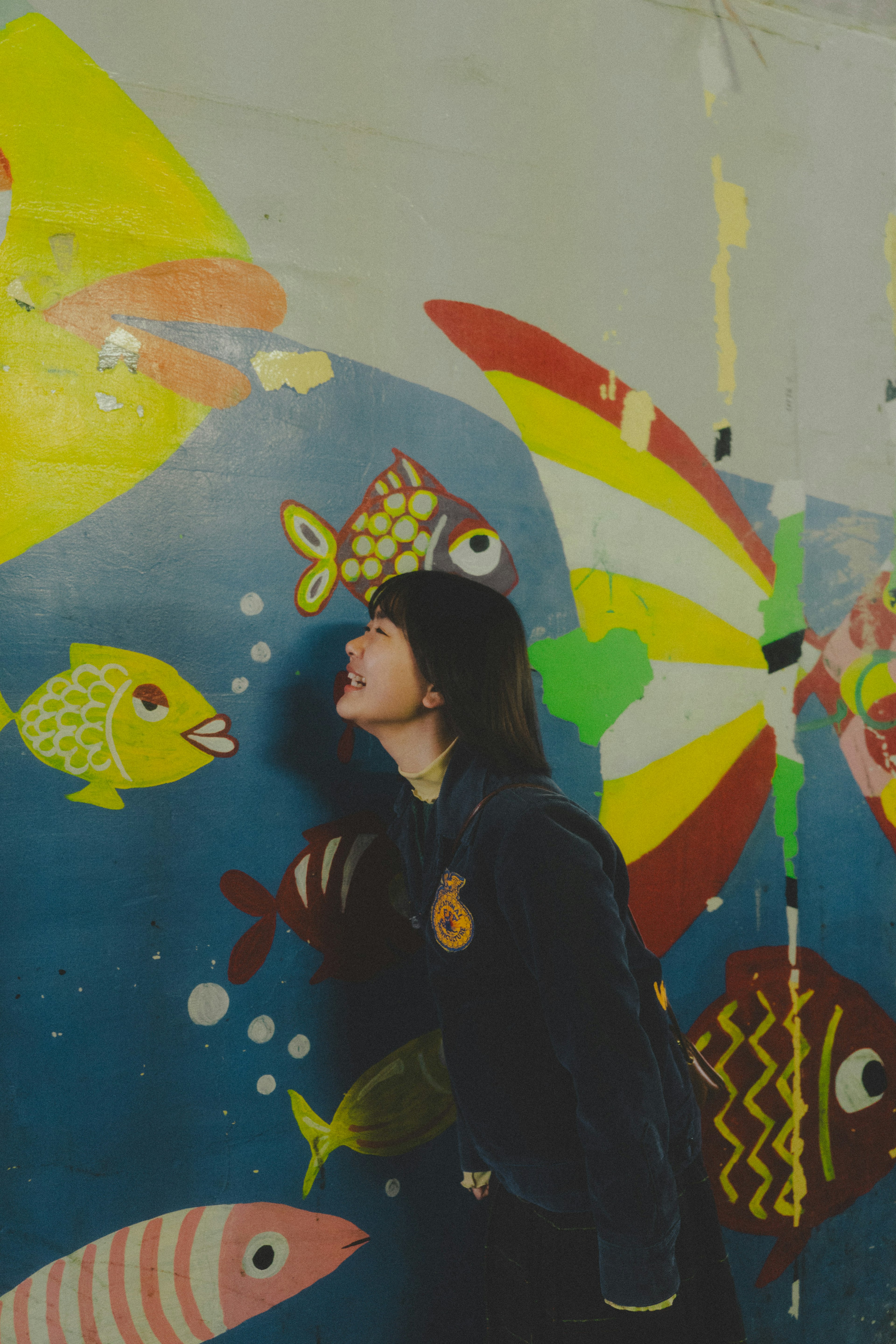 A woman smiling in front of a colorful fish mural