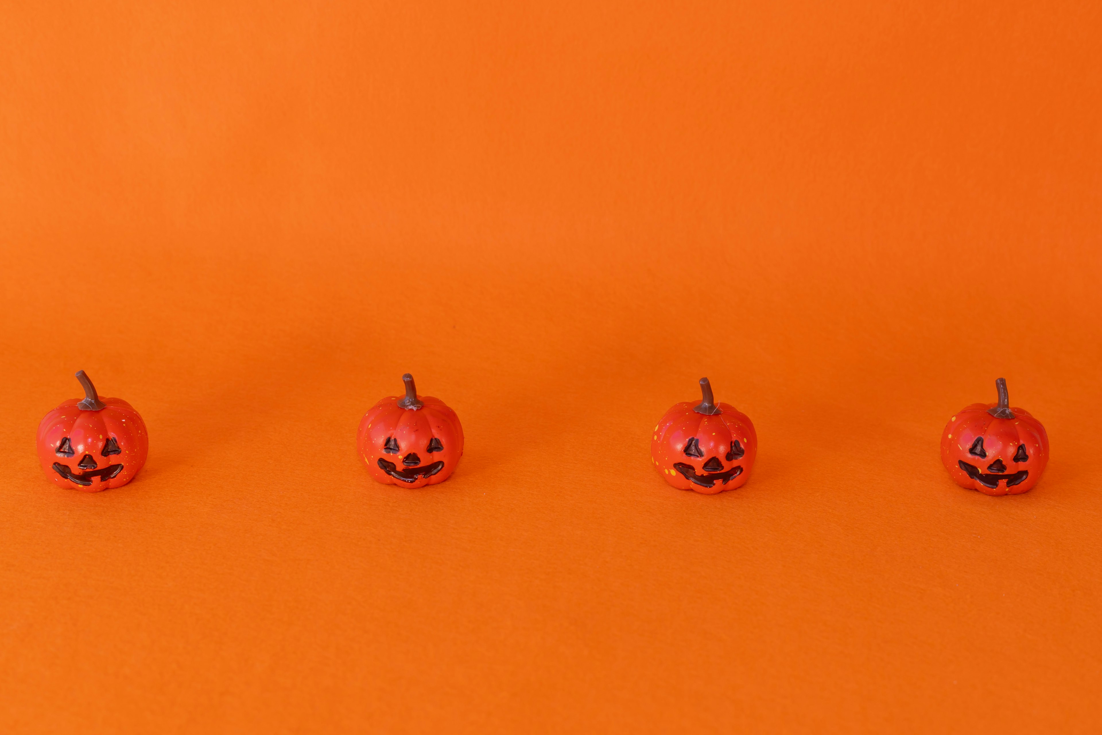 Quatre citrouilles décorées alignées sur un fond orange