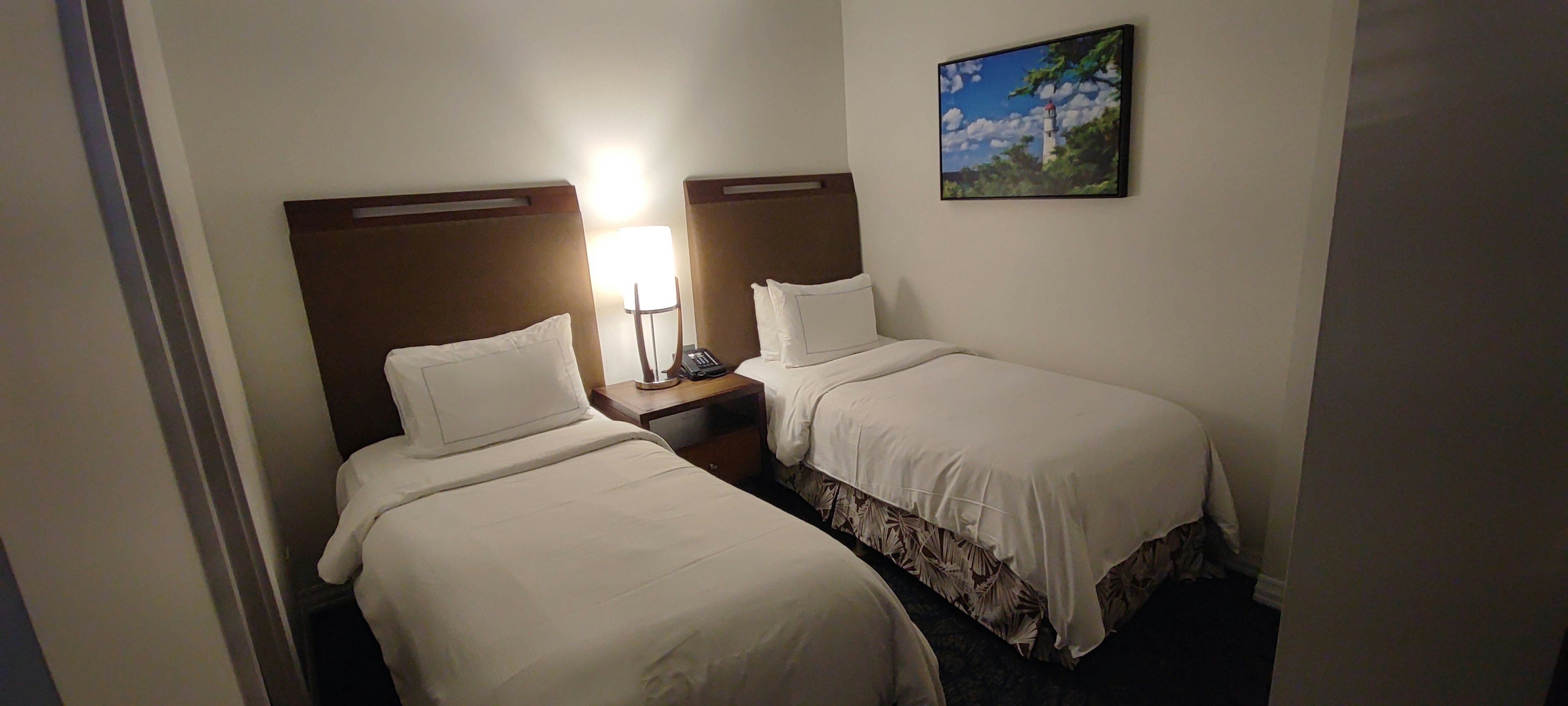 Simple guest room with two white beds and a lamp