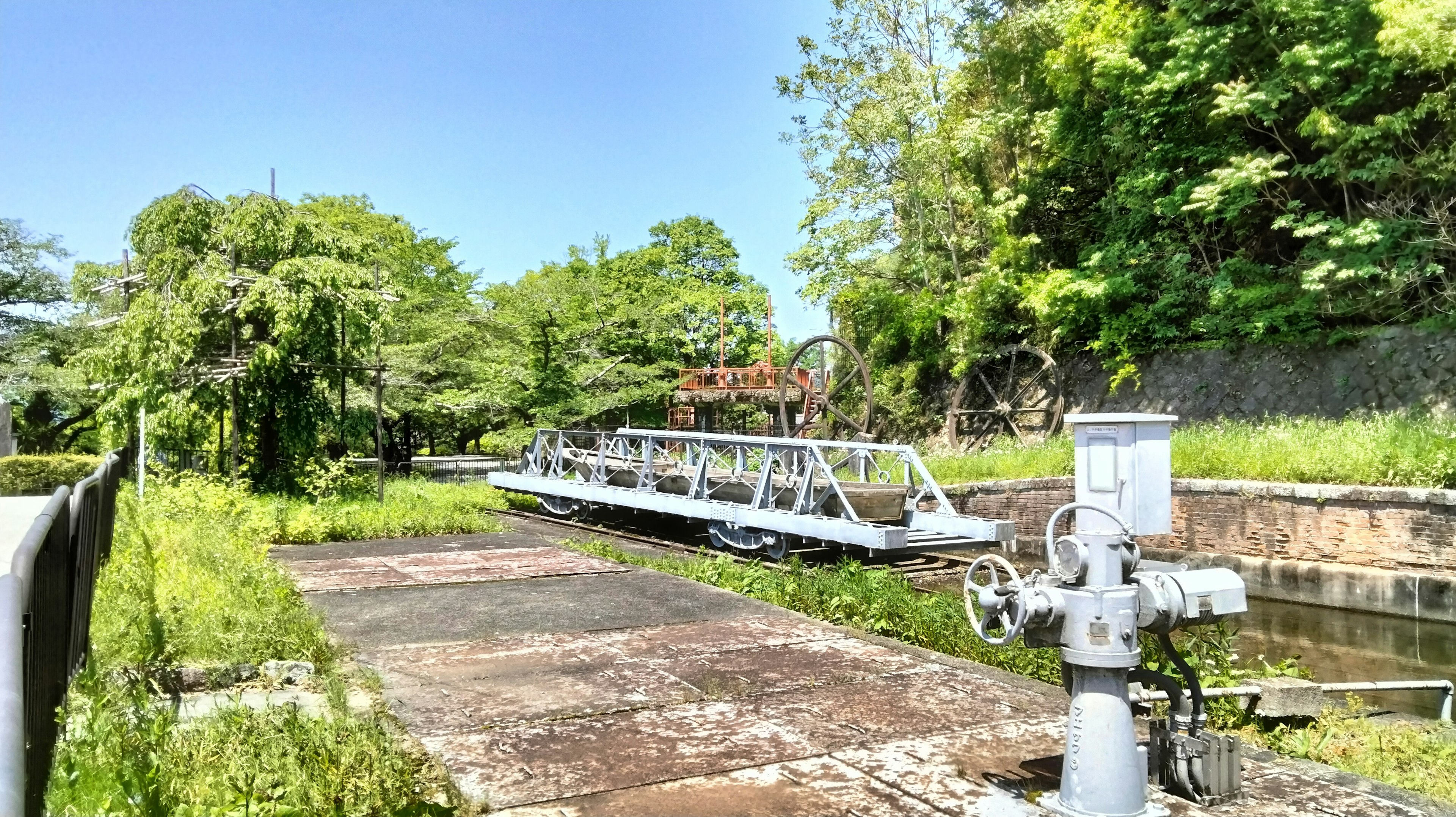 A serene waterway surrounded by lush greenery with a white bridge A water control device is positioned beside the bridge