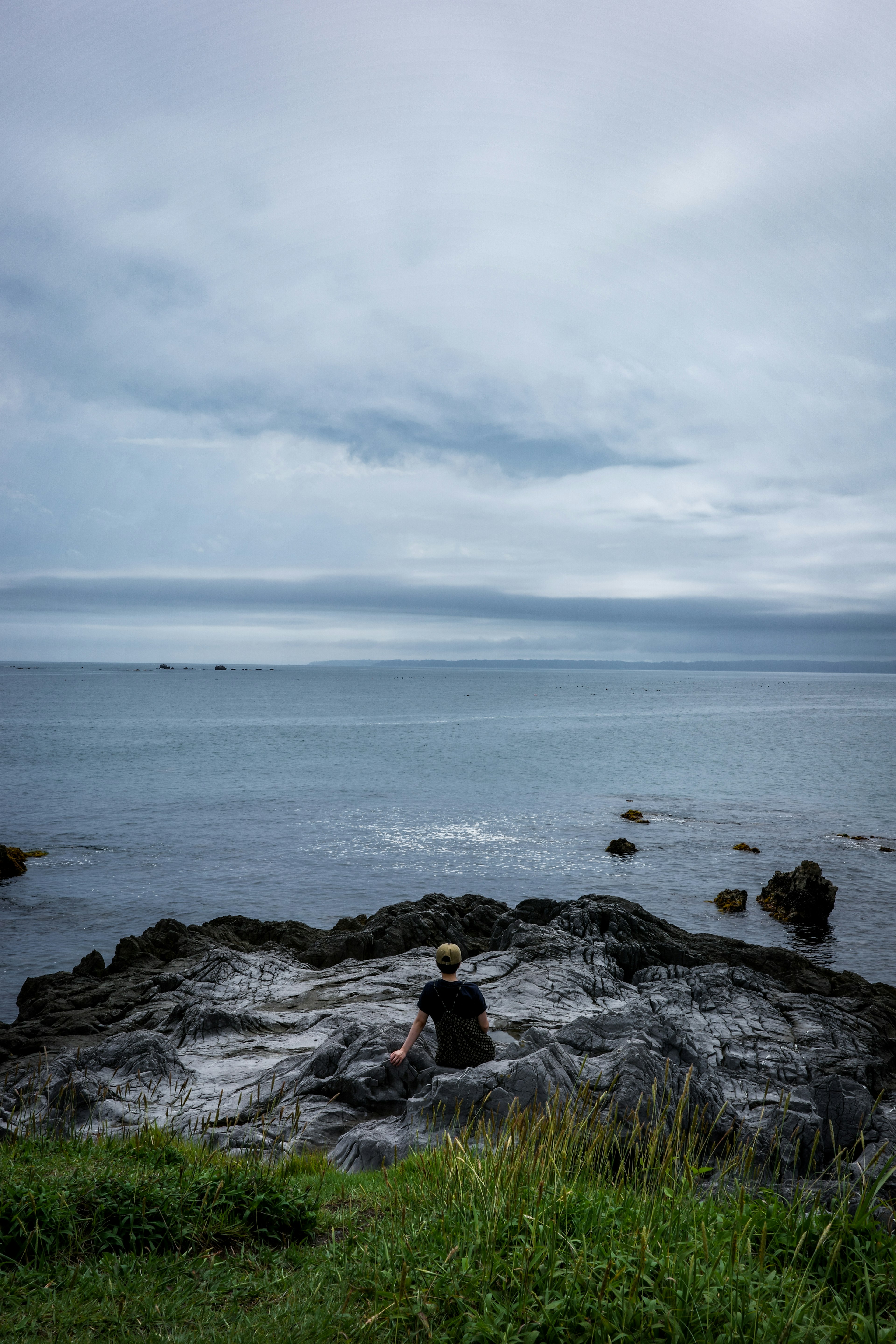 Person sitzt auf Felsen am Meer unter einem bewölkten Himmel