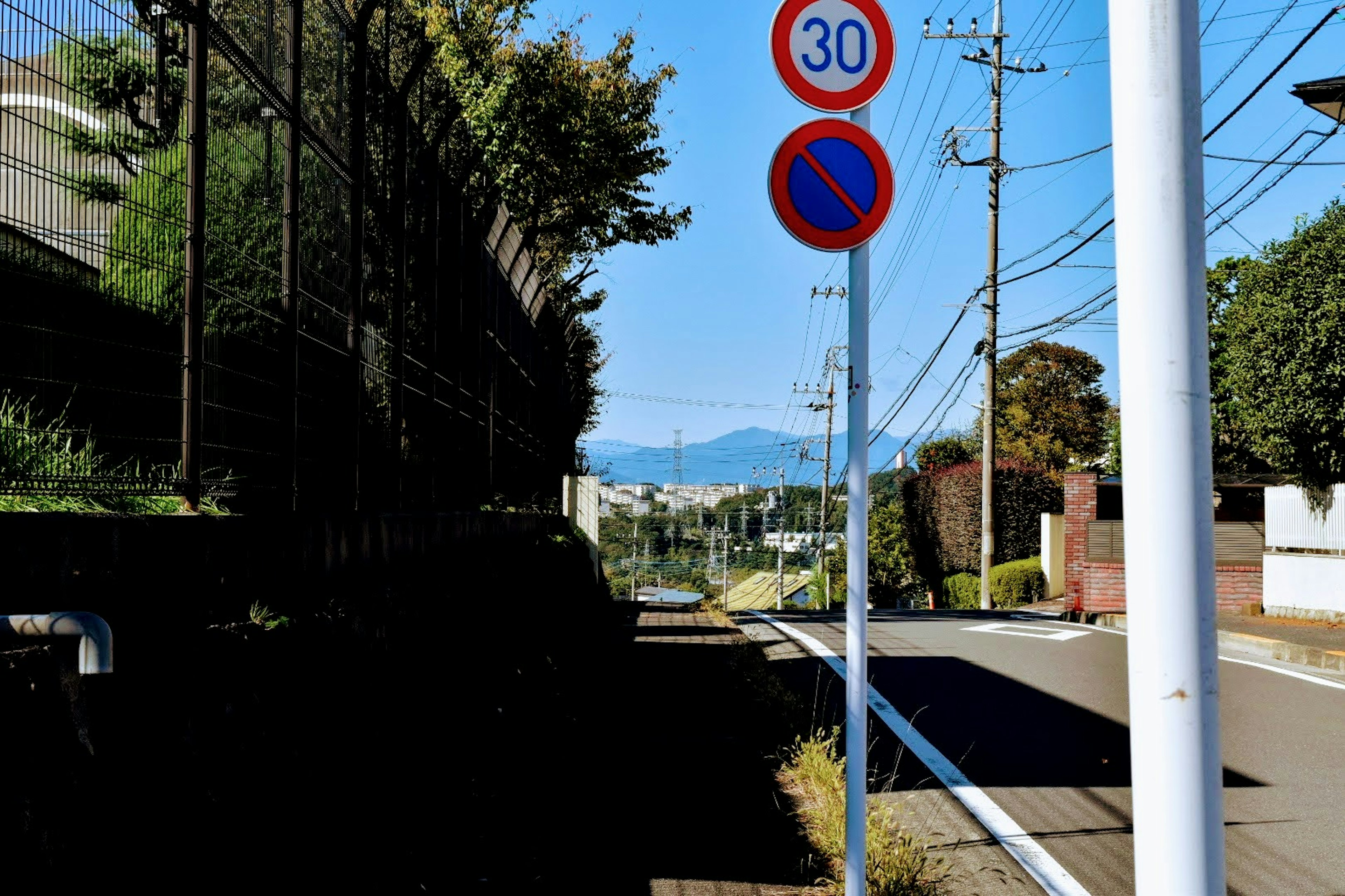 Una scena di strada tranquilla con cielo blu e montagne visibili segnali stradali e pali della luce presenti